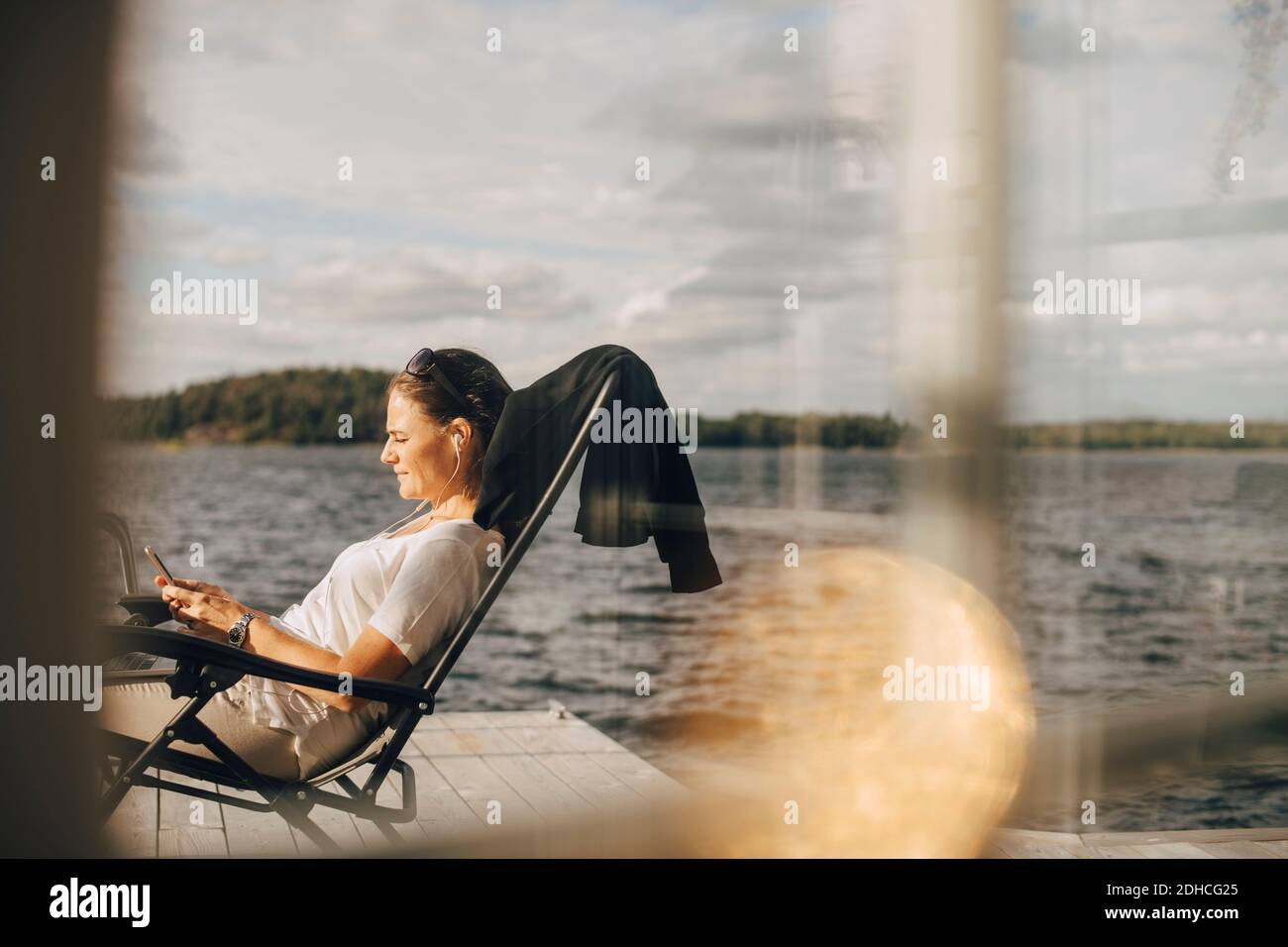 Vue latérale d'une femme portant un casque lorsque le téléphone est allumé patio vu par la fenêtre Banque D'Images