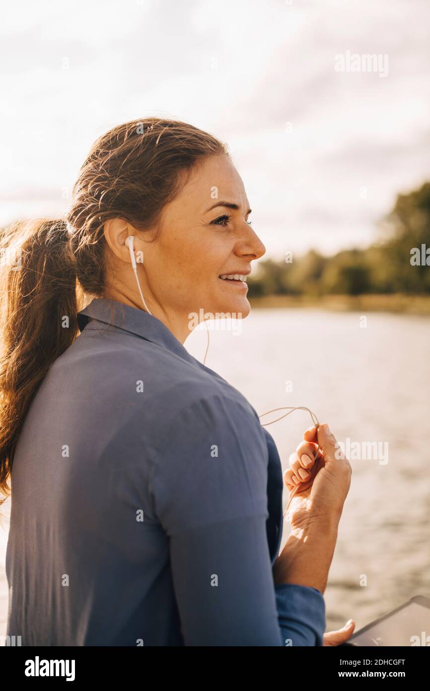 Femme souriante parlant avec un casque via une tablette numérique via un casque assis au bord du lac Banque D'Images