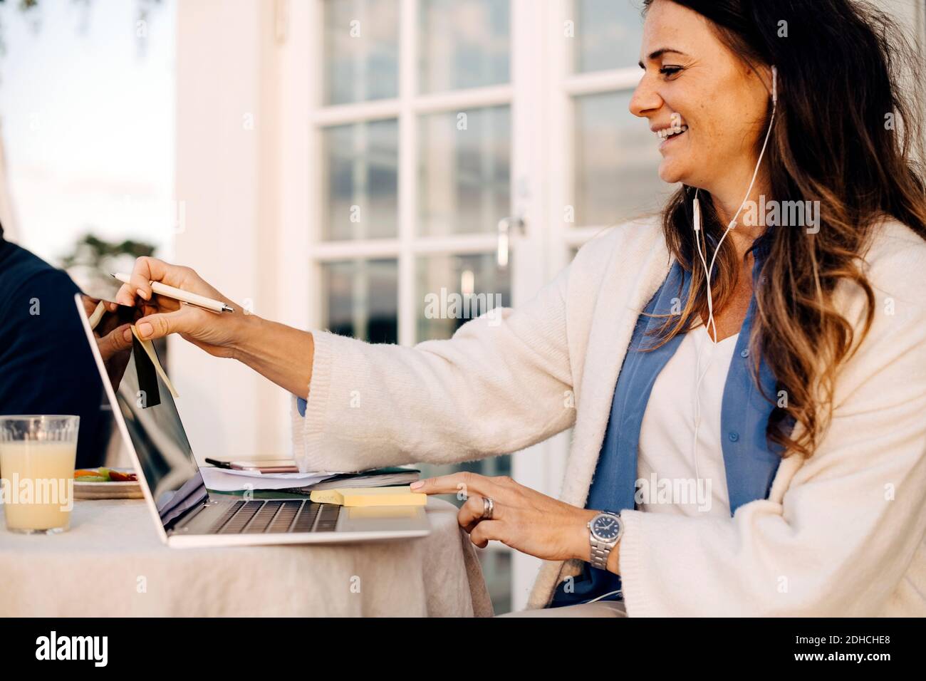 Femme mûre souriante portant un casque tout en utilisant un ordinateur portable en vacances villa Banque D'Images