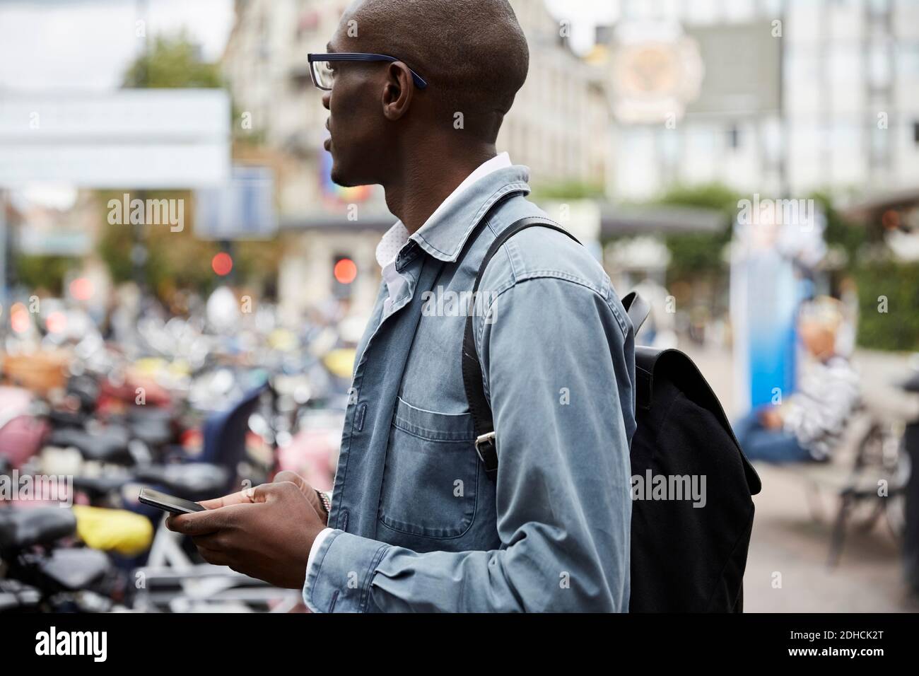 Vue latérale d'un homme d'affaires de taille moyenne, vue sur l'extérieur pendant qu'il se tient debout avec smartphone en ville Banque D'Images