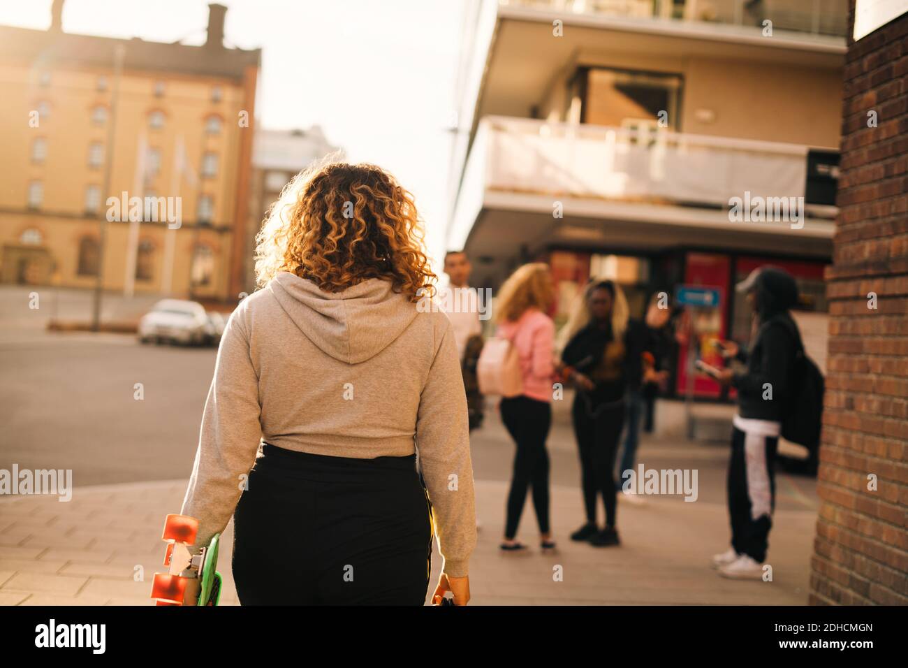 Vue arrière d'une femme avec skateboard en direction de ses amis ville Banque D'Images