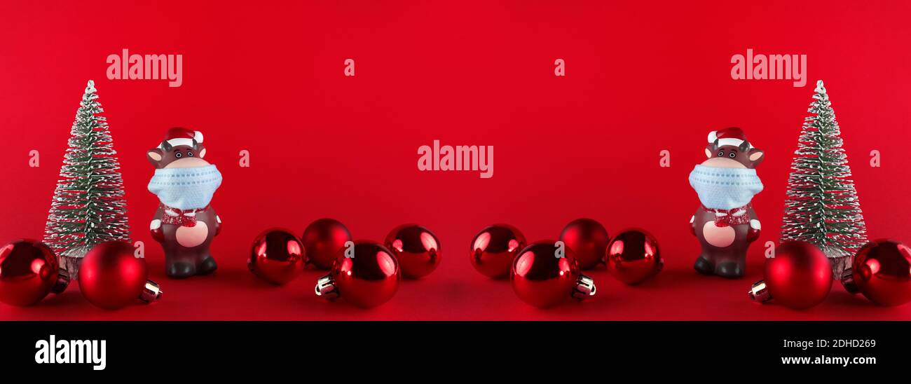 Statuettes en céramique d'Ox dans un masque médical, arbres de Noël et boules sur le dos rouge. Bannière large avec espace de copie. Symbole du nouvel an 2021. Banque D'Images