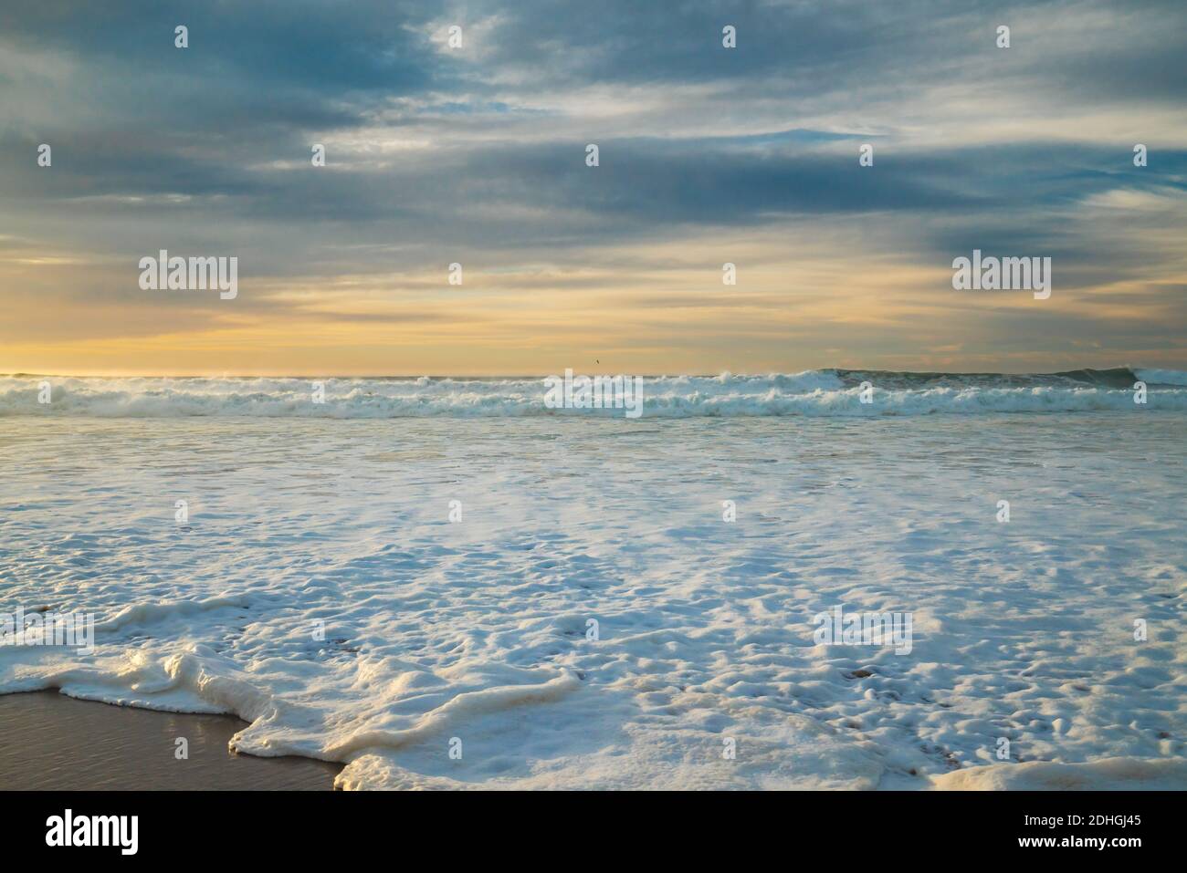 Coucher de soleil sur la mer. Vagues orageux et mousse de mer sur la plage avec un ciel nuageux magnifique sur fond Banque D'Images