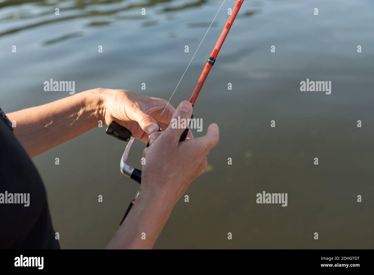 Les mains du pêcheur tiennent un tournant au-dessus de l'eau pendant la pêche. Banque D'Images