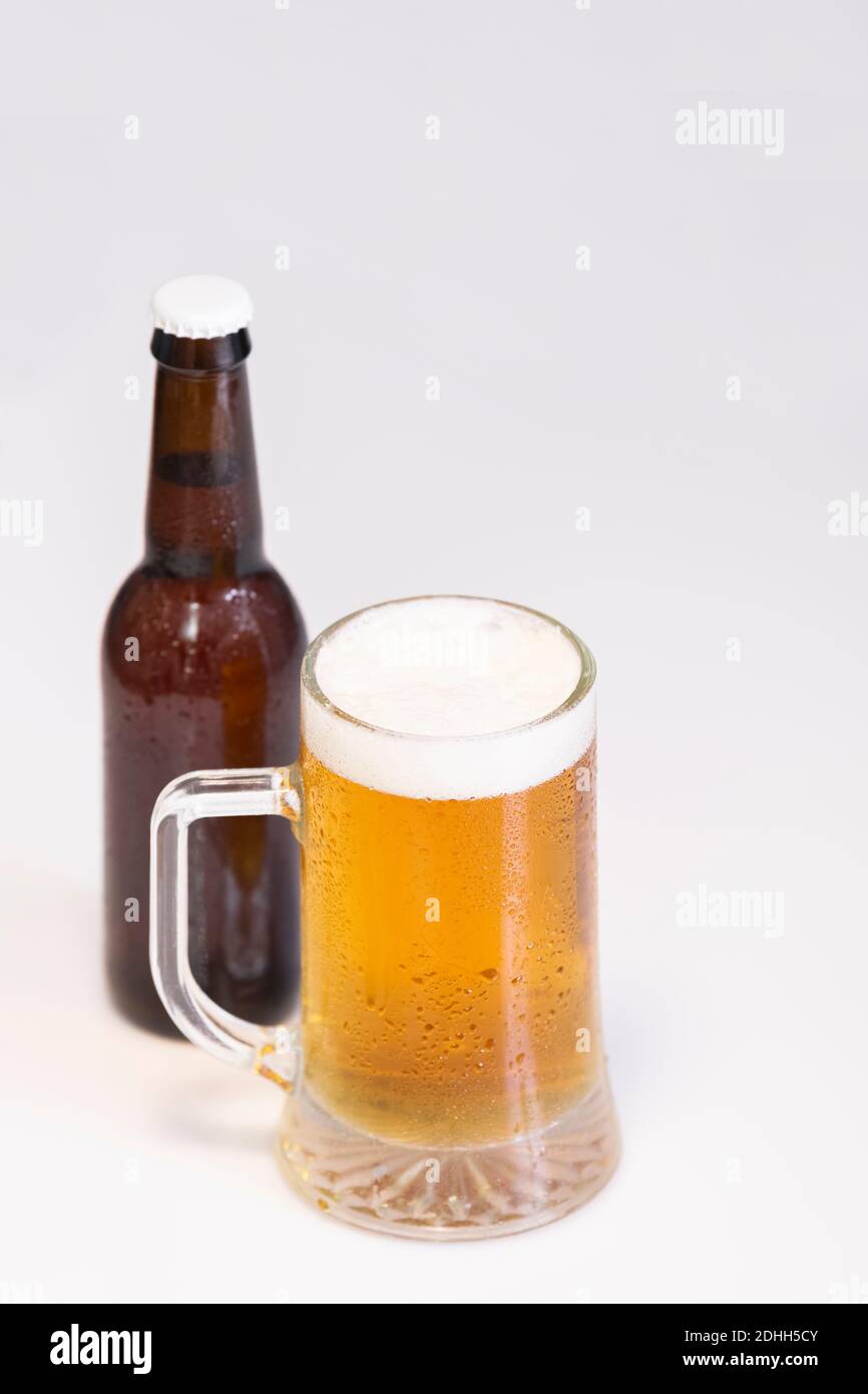Mise au point sélective d'une tasse de bière froide appétissante avec une bouteille de bière non focalisée à l'arrière sur un fond clair. Concept bière et loisirs. Banque D'Images