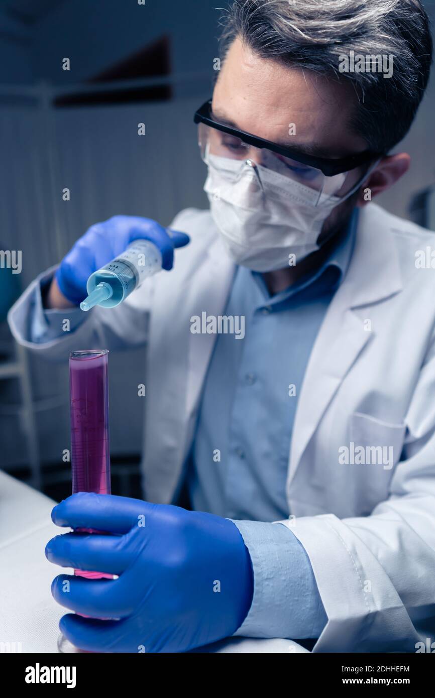 Un jeune scientifique regarde un tube à essai en laboratoire. L'homme porte des lunettes de protection Banque D'Images