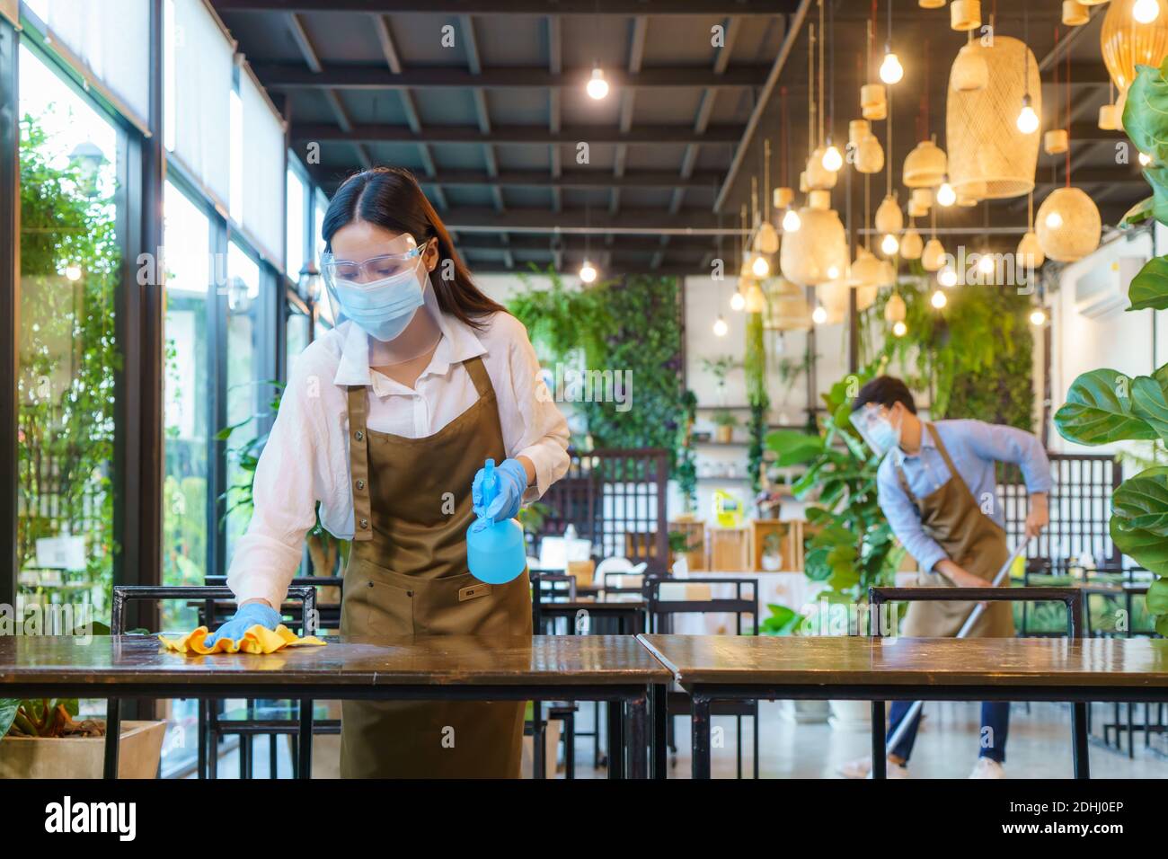 Portrait un employé de restaurant asiatique attrayant porte un masque et un visage nettoyer la table et le sol avec de l'alcool et un chiffon humide avant la crème de bienvenue Banque D'Images