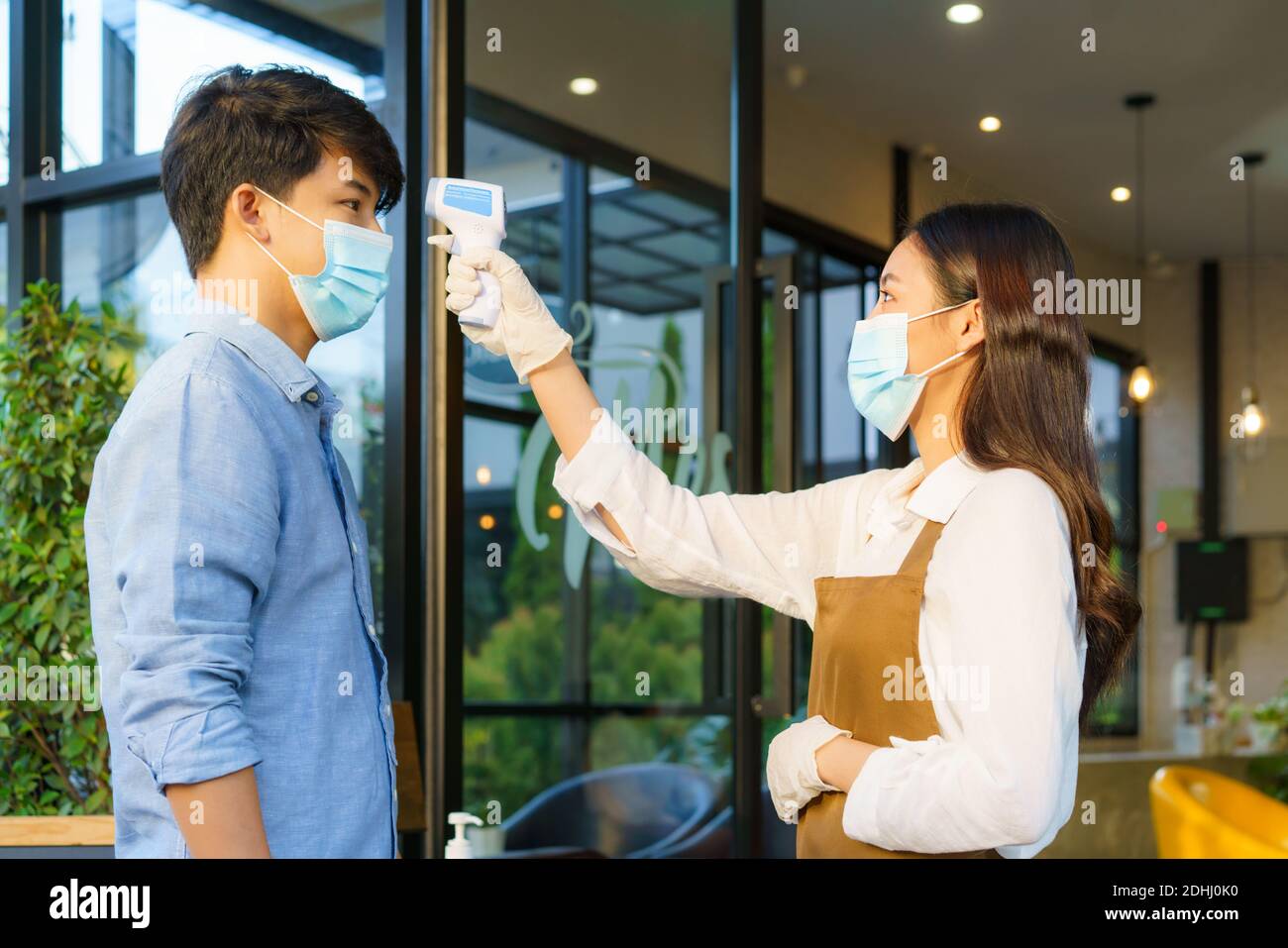 Femme asiatique employé de café après prendre la température homme asiatique avec masque avant d'aller au restaurant ou au café pour nouveau coronavirus de style de vie normal Banque D'Images