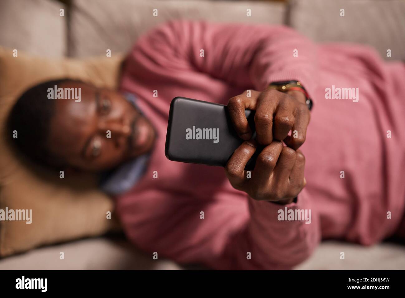 Vue en grand angle de l'homme africain tapant sur un téléphone portable travailler en ligne en étant allongé sur un canapé Banque D'Images