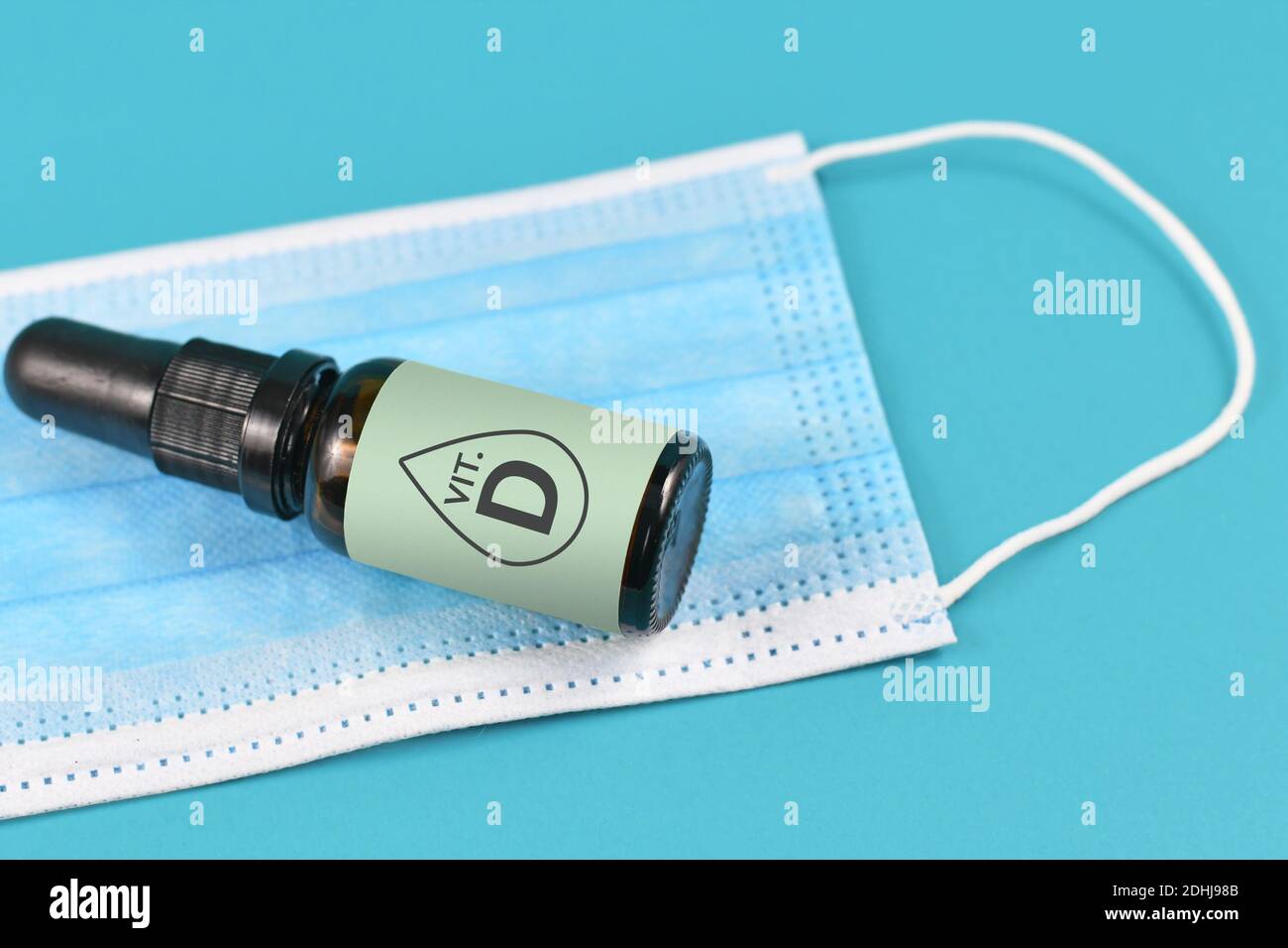 Concept pour la vitamine D aider à combattre la maladie du virus Corona avec masque médical et flacon avec gouttes de vitamine sur bleu arrière-plan Banque D'Images