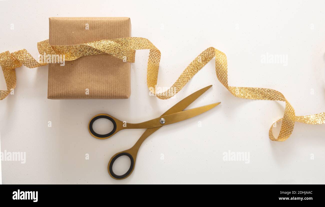 Cadeaux de Noël emballage maison, préparation des vacances. Faire un noeud  avec un ruban or brillant, la décoration d'une boîte cadeau en papier brun.  Package et scor Photo Stock - Alamy