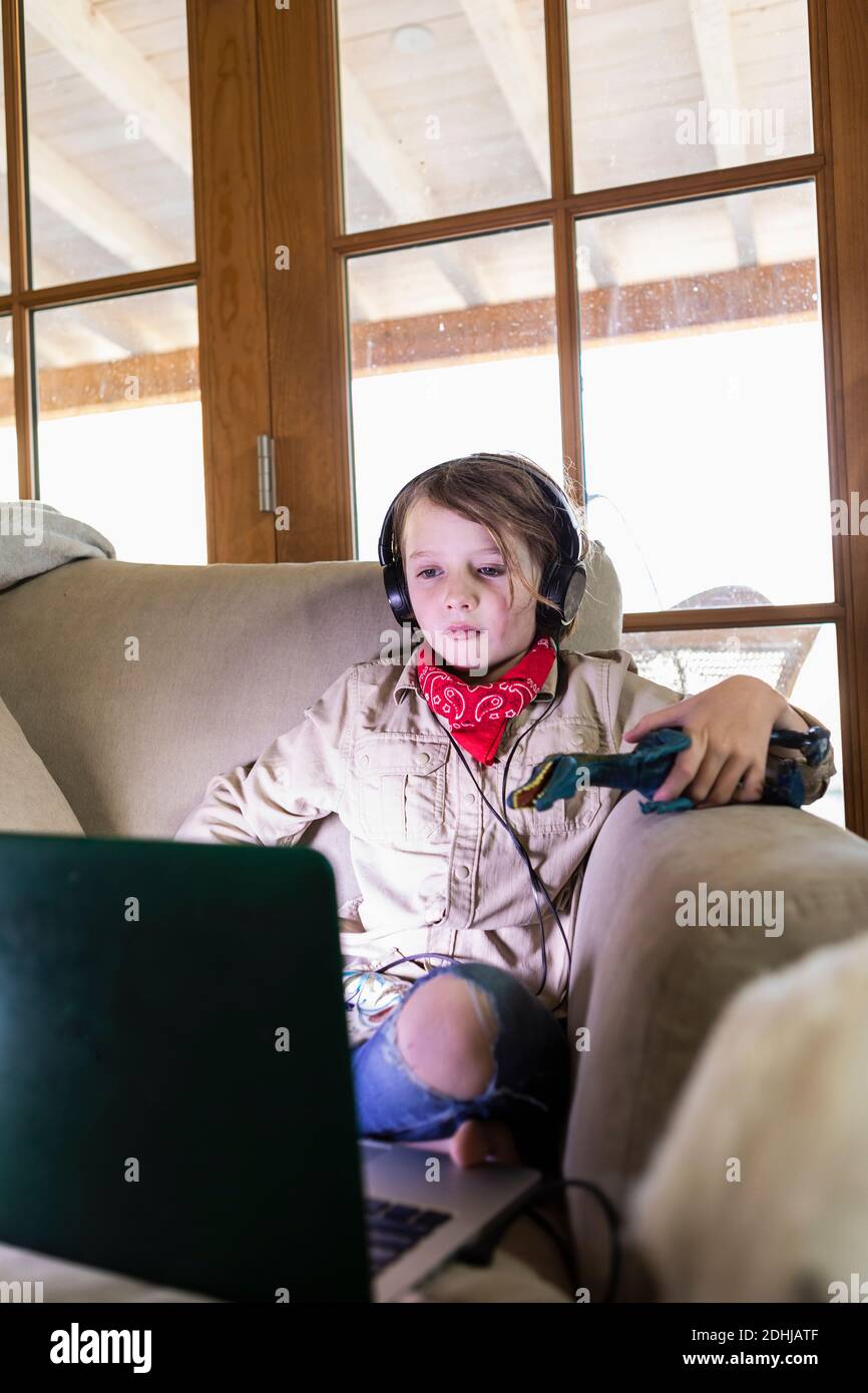 jeune garçon portant une tenue safari et un casque pour regarder un film sur ordinateur portable Banque D'Images