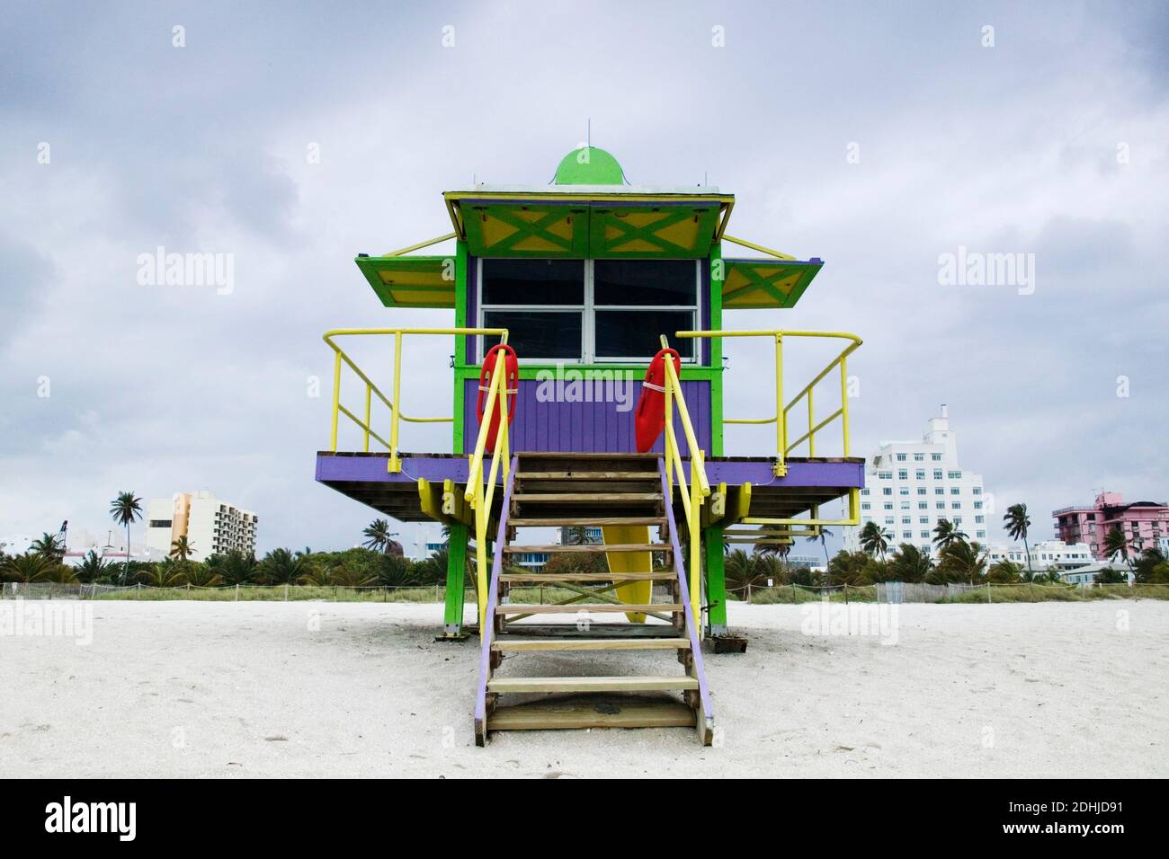 Refuge de sauveteurs en bois coloré sur une plage de sable avec des bâtiments élevés au-delà. Banque D'Images