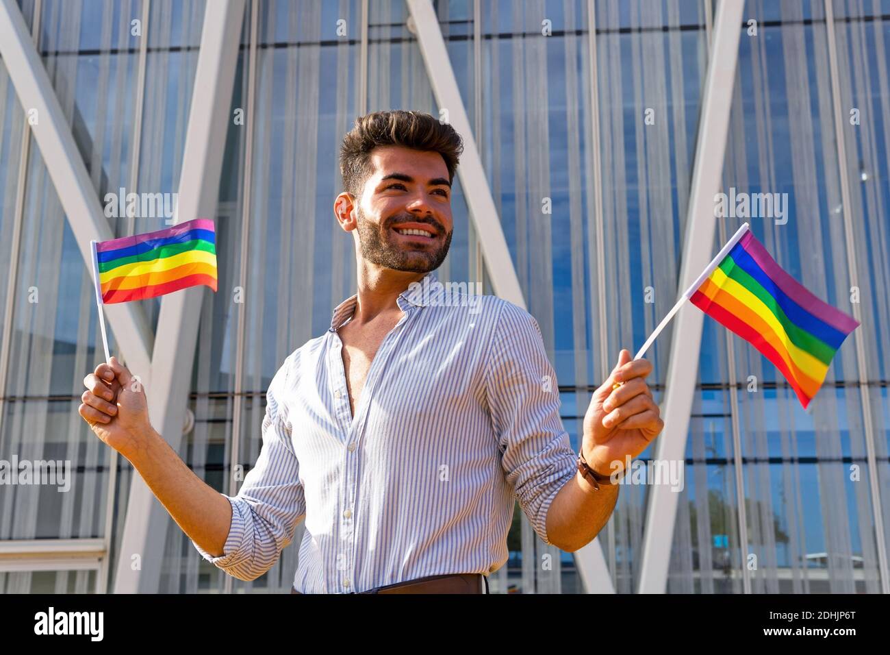 Faible angle de l'homosexuel ravie mâle debout dans la rue avec Paper les drapeaux LGBT et regarder loin Banque D'Images