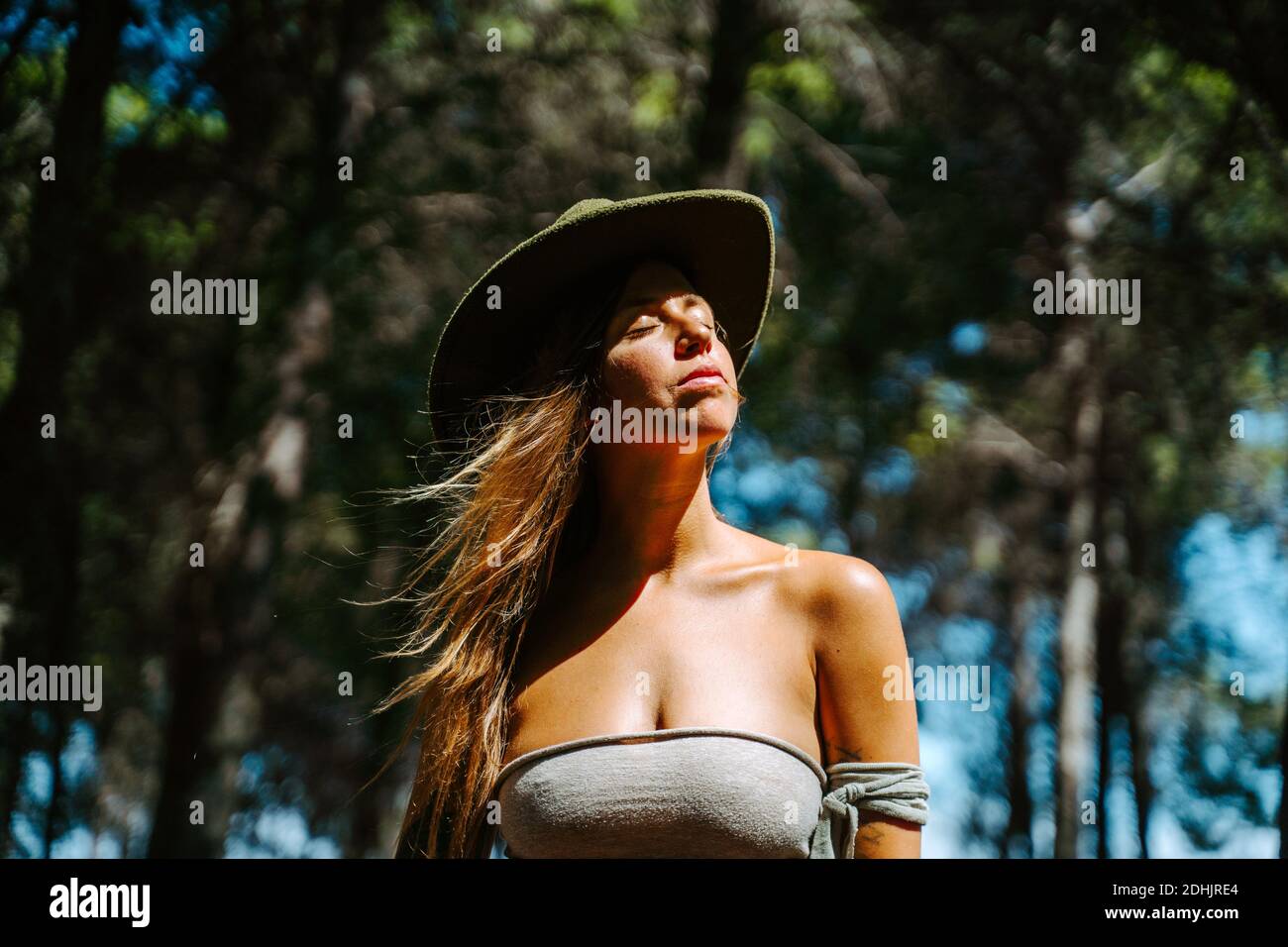 Hippie féminine douce en chapeau et debout en bois et profiter de la lumière du soleil avec les yeux fermés Banque D'Images