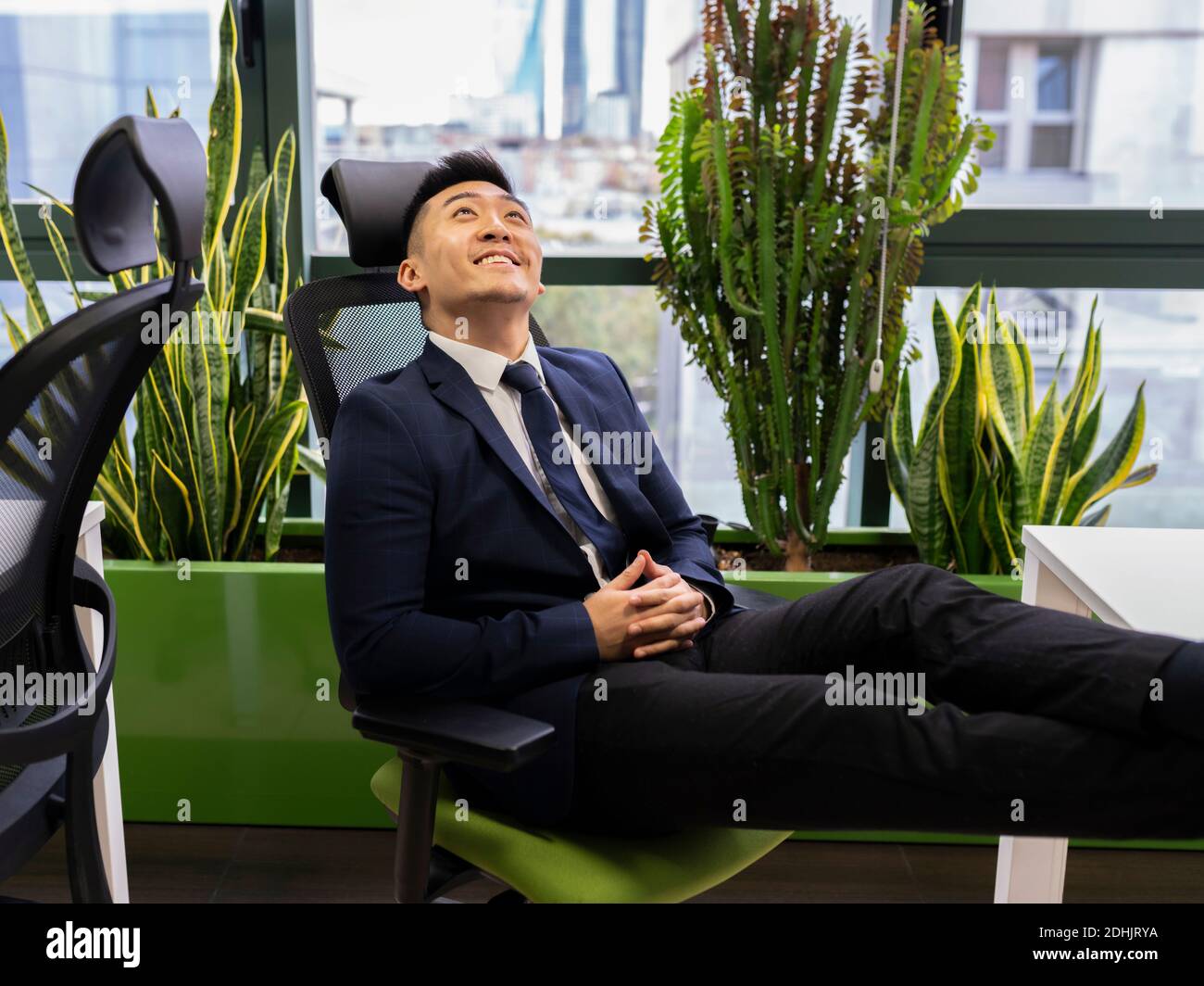 Vue latérale d'un jeune homme d'affaires asiatique en costume formel vous cherchez à sourire et à rêver tout en pensant à la réussite de vos affaires stratégie en mo Banque D'Images