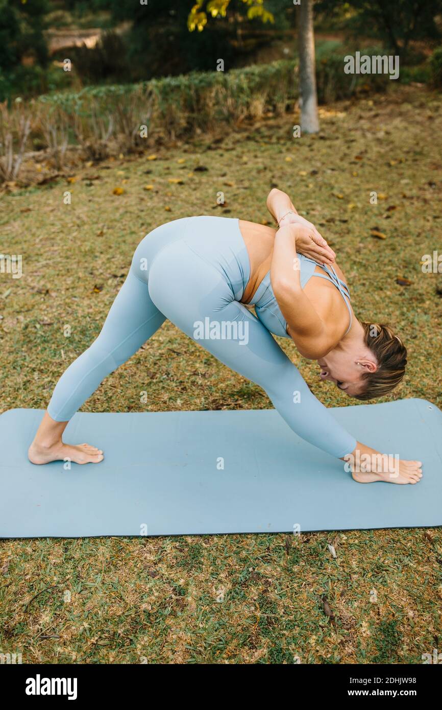 De dessus de la femme mince dans les vêtements de sport faisant la moitié Pyramide Posez avec les mains de prière derrière le dos tout en pratiquant le yoga nature Banque D'Images