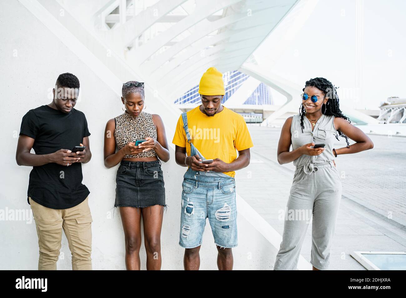 Jeunes gens noirs dans des vêtements élégants debout en zone urbaine et la messagerie sur les réseaux sociaux via les smartphones Banque D'Images