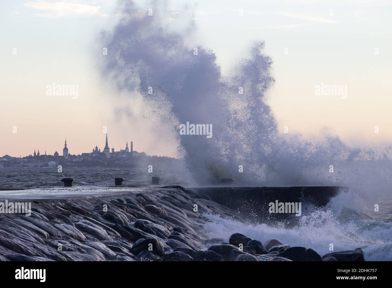 Vagues de tempête écrasant avec de grandes éclaboussures sur le brise-lames sur la mer avec la silhouette lointaine de la ville couleur du coucher de soleil de la Tallinn, consistant Banque D'Images