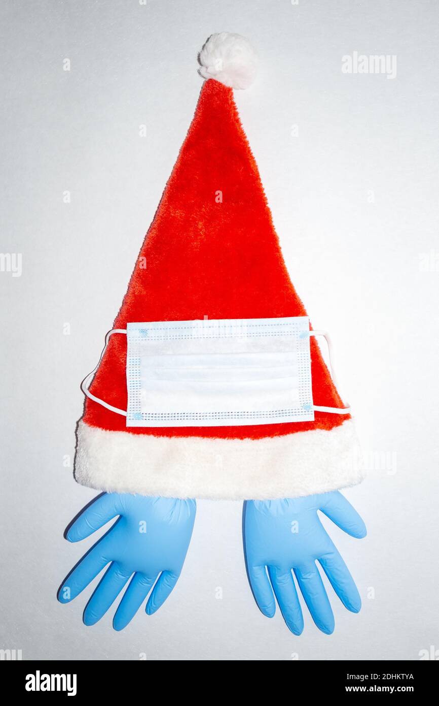 Chapeau de Noël en peluche rouge et blanc avec masque chirurgical et une paire de gants médicaux en vinyle bleu gonflé. Vue verticale du dessus Banque D'Images