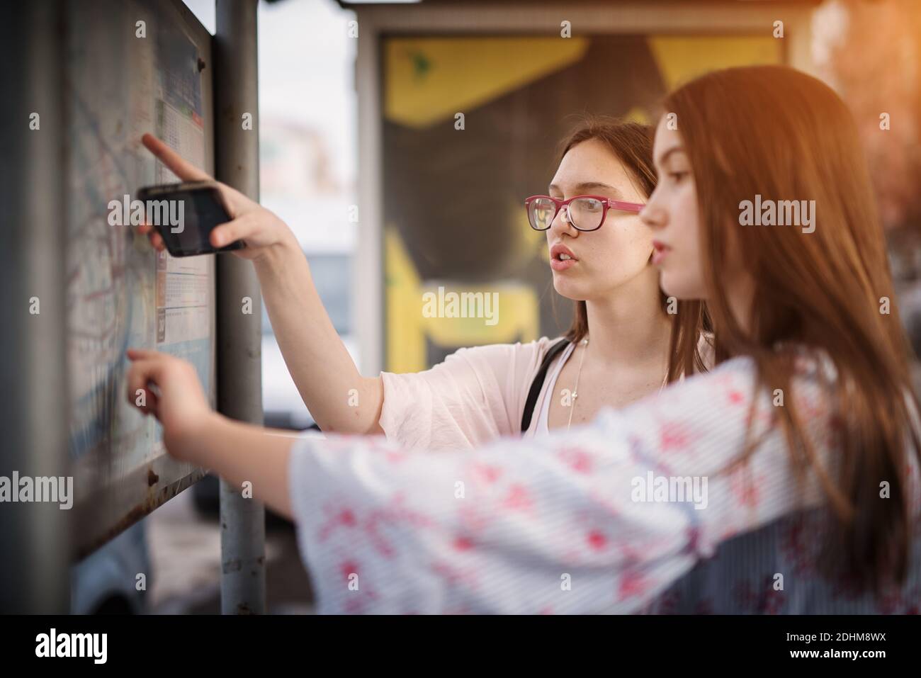Deux jolies lycéennes attendent un bus et font un plan de temps tout en regardant sur la carte de la ville. Banque D'Images