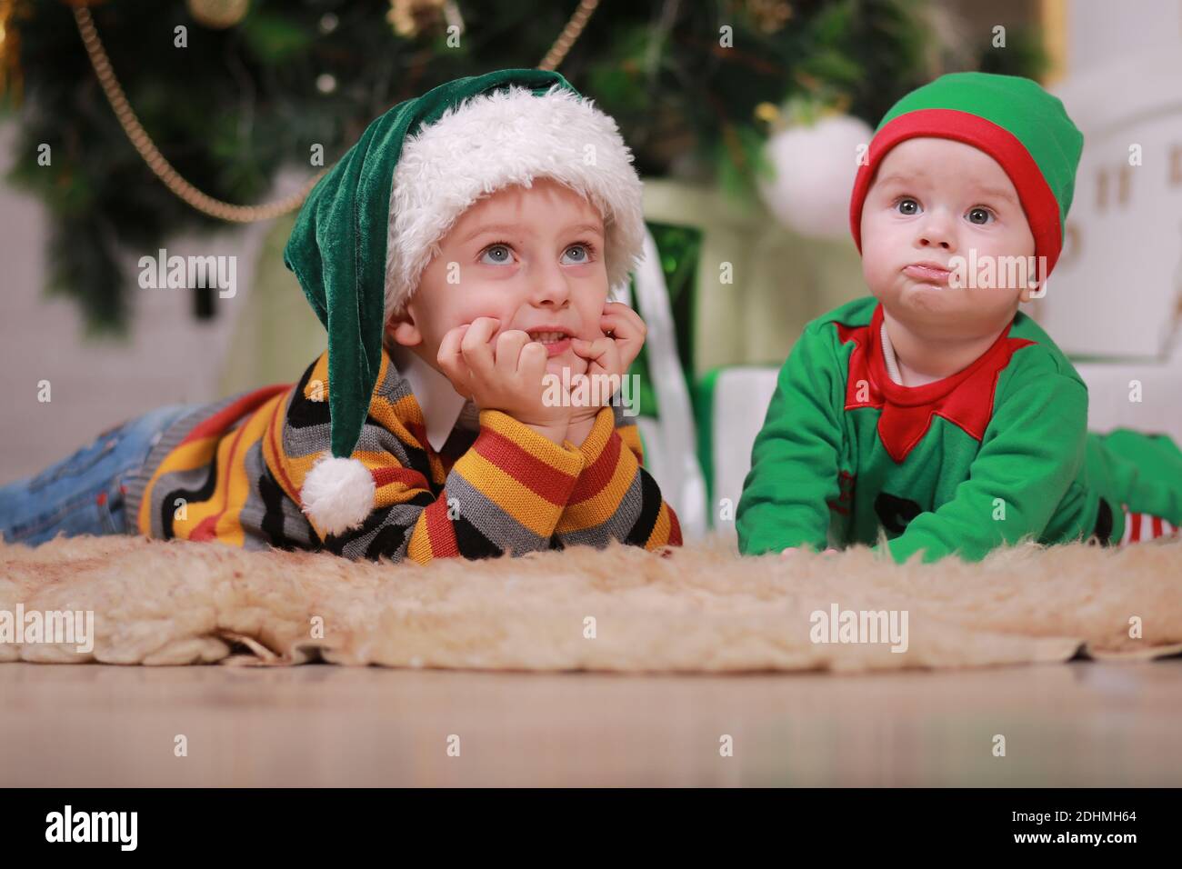 Bébé garçon en costume d'orf vert rouge avec son frère aîné en chapeau de  père noël assis sous l'arbre de Noël et des boîtes-cadeaux Photo Stock -  Alamy