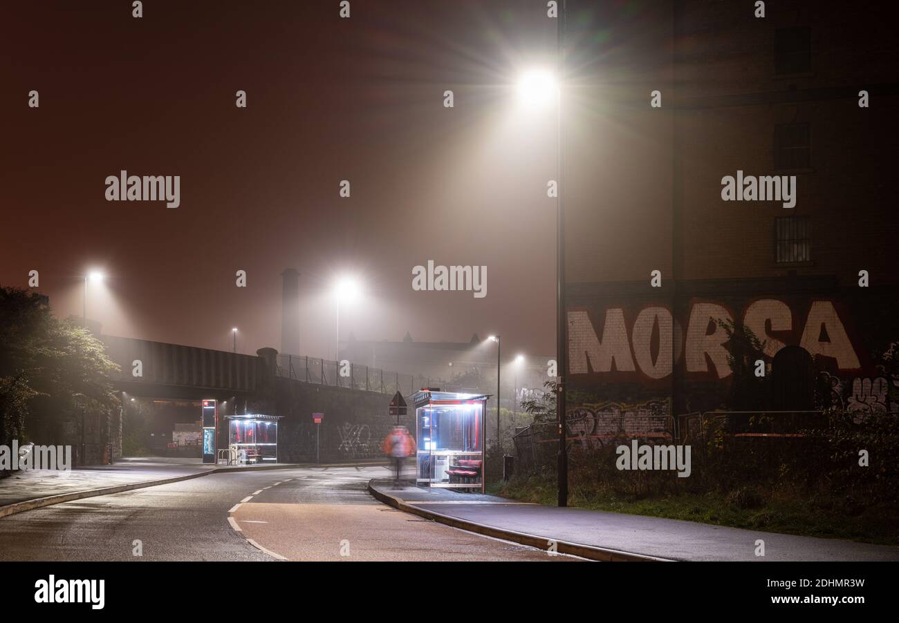 Un passager attend à l'arrêt de Cumberland Basin Metrobus pendant une nuit d'automne brumeuse sur la ligne de bus South Bristol. Banque D'Images