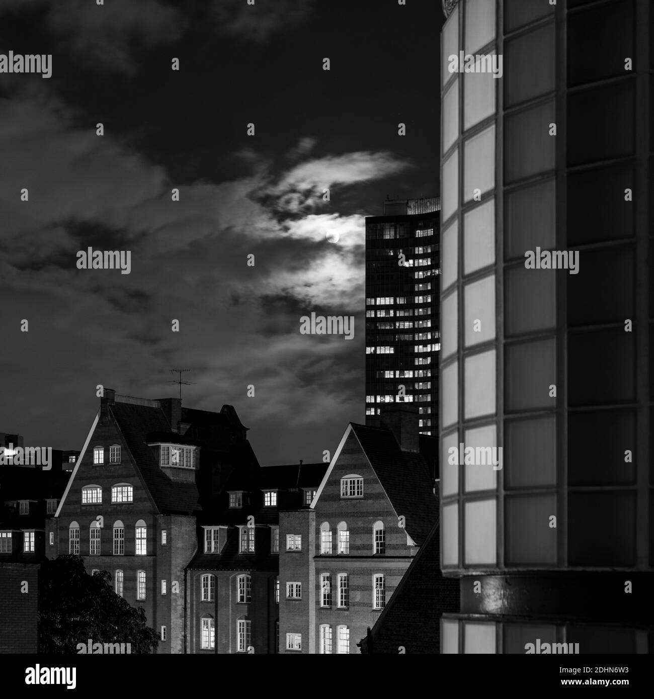 vue en noir et blanc sur les nuages au clair de lune vieux bâtiment en briques rouges la nuit avec des bâtiments modernes en arrière-plan Banque D'Images