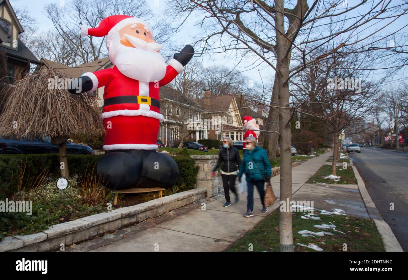 Toronto, Canada. 11 décembre 2020. Les gens qui portent des masques faciaux marchent devant un père Noël gonflable géant sur Inglewood Drive à Toronto, Canada, le 11 décembre 2020. À partir de 2013, des dizaines de Santa Cclauses gonflables de 14 mètres de haut s'étendent le long de Inglewood Drive à Toronto pendant la saison des fêtes, attirant de nombreux visiteurs. Credit: Zou Zheng/Xinhua/Alamy Live News Banque D'Images