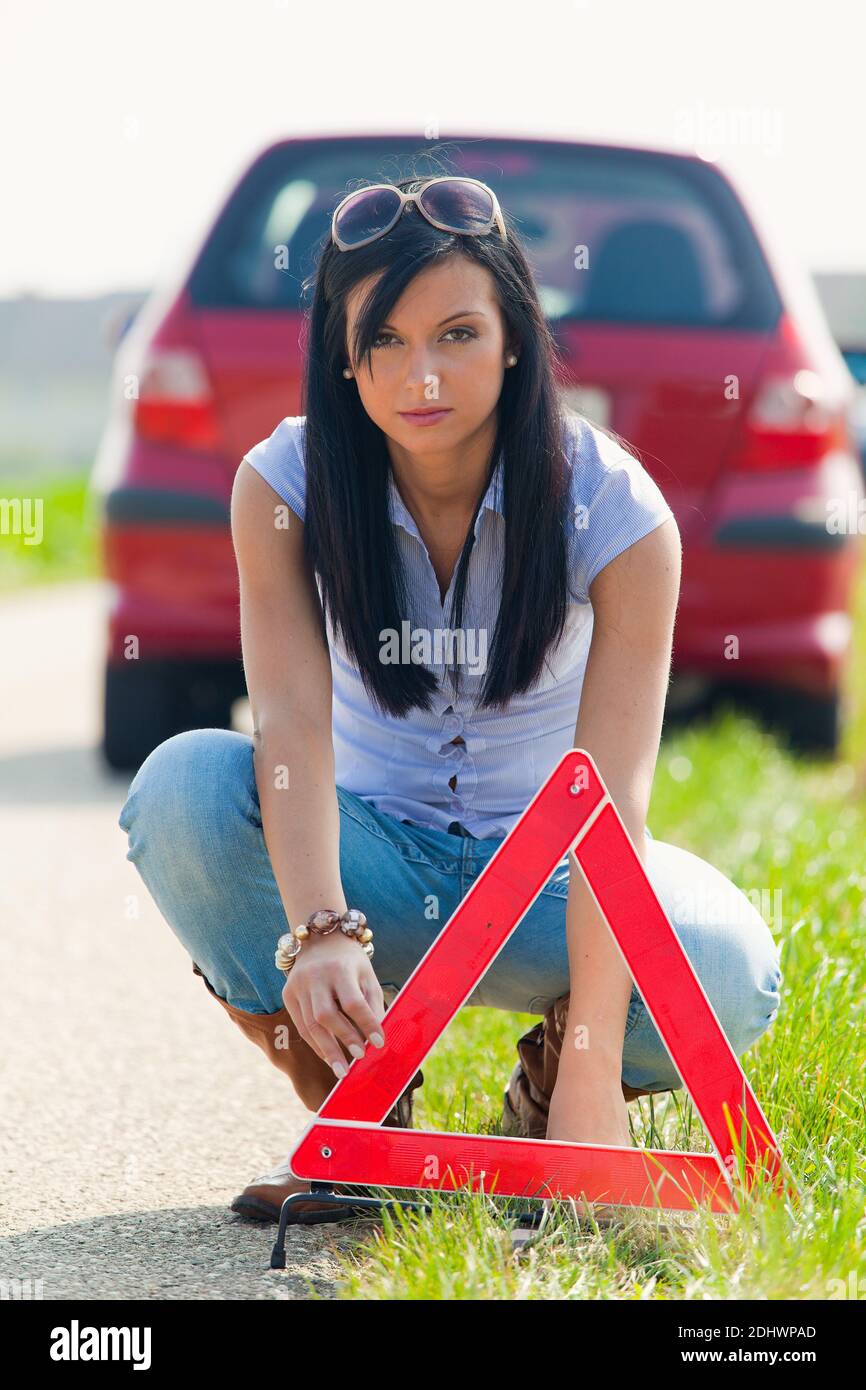 Junge Frau mit einer Reifenpanne am Auto, Warnkreuz wird aufgestellz, Banque D'Images