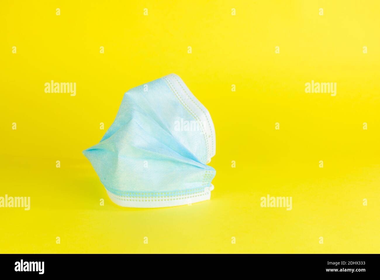 Un masque protecteur bleu, à moitié froissé, sur un fond jaune Uni. Banque D'Images