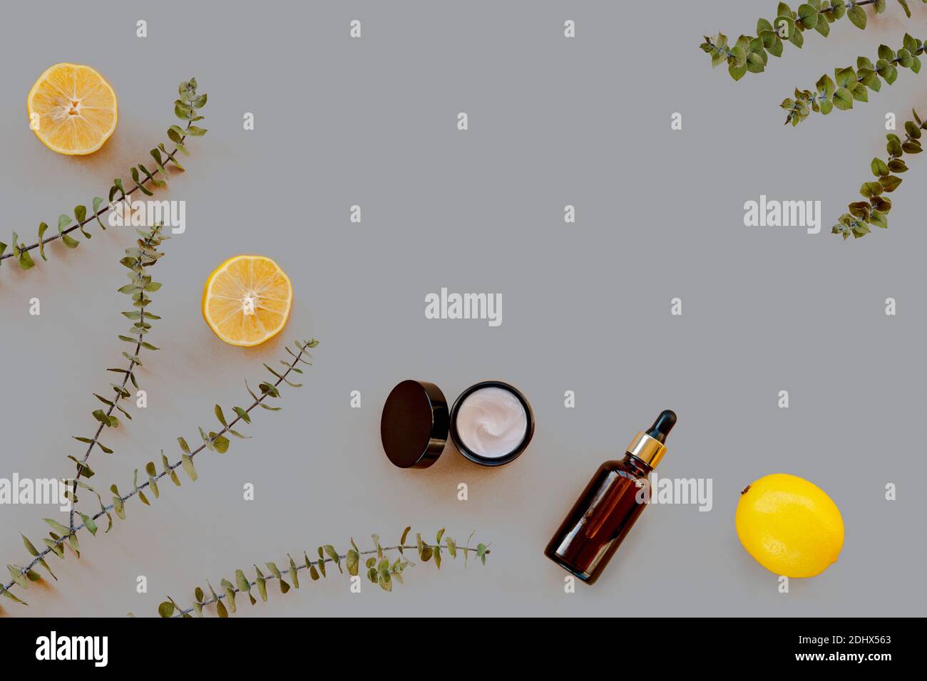 Bouteilles en verre sans marque, fruits jaunes au citron et branches d'eucalyptus sur fond gris. Concept de spa à la maison. Vue de dessus, plat, espace de copie. Couleur 2021 Banque D'Images