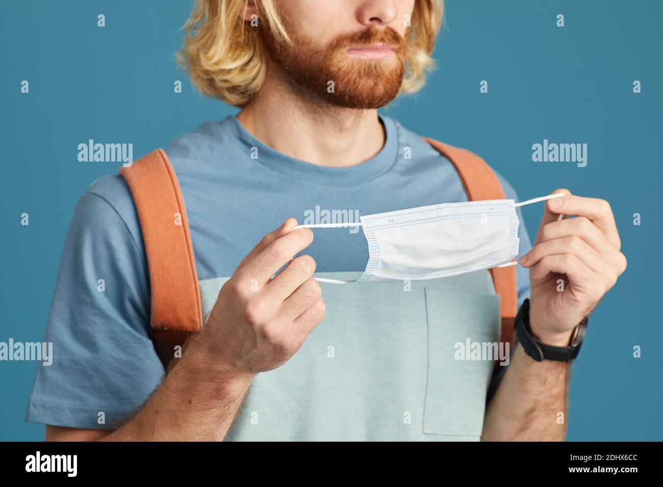 Gros plan d'un jeune homme avec sac à dos derrière son dos masque de protection isolé sur fond bleu Banque D'Images