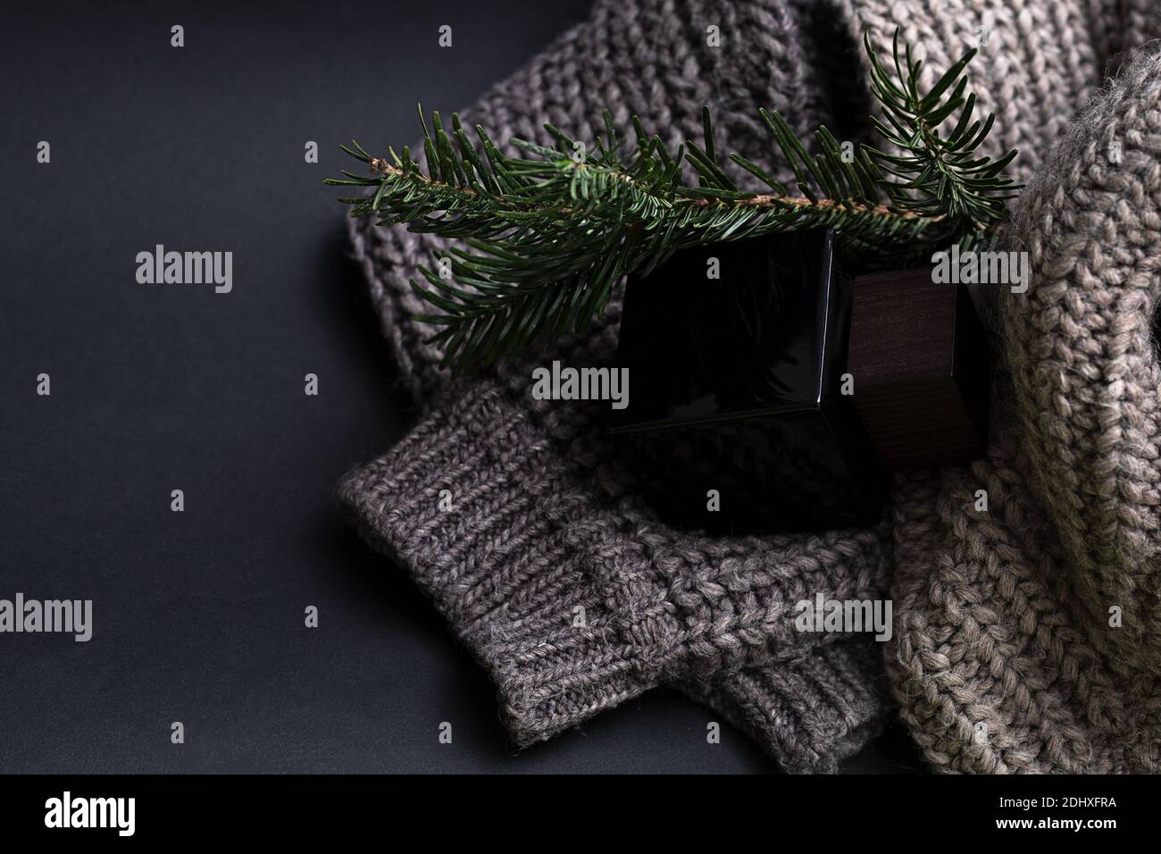 Parfum masculin sur fond noir dans un pot en verre noir avec un couvercle en bois. À proximité se trouve un pull en tricot grossier et une branche de conifères. Concept de cadeau Banque D'Images