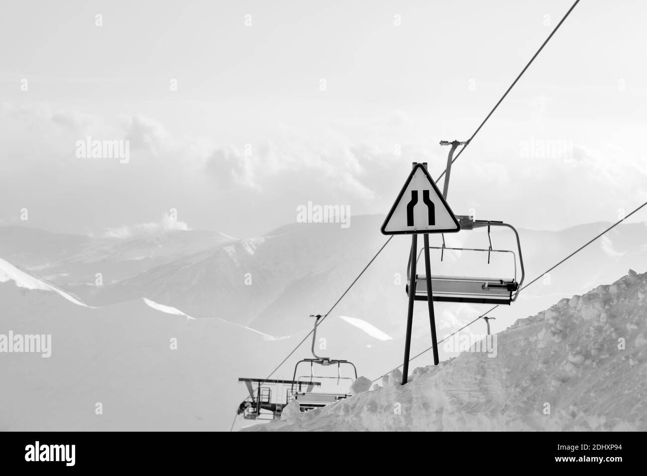 Avertissement signalisation routière rocade, télésiège et hautes montagnes enneigées dans le brouillard en arrière-plan. Montagnes du Caucase en soirée d'hiver. Géorgie région Gudau Banque D'Images
