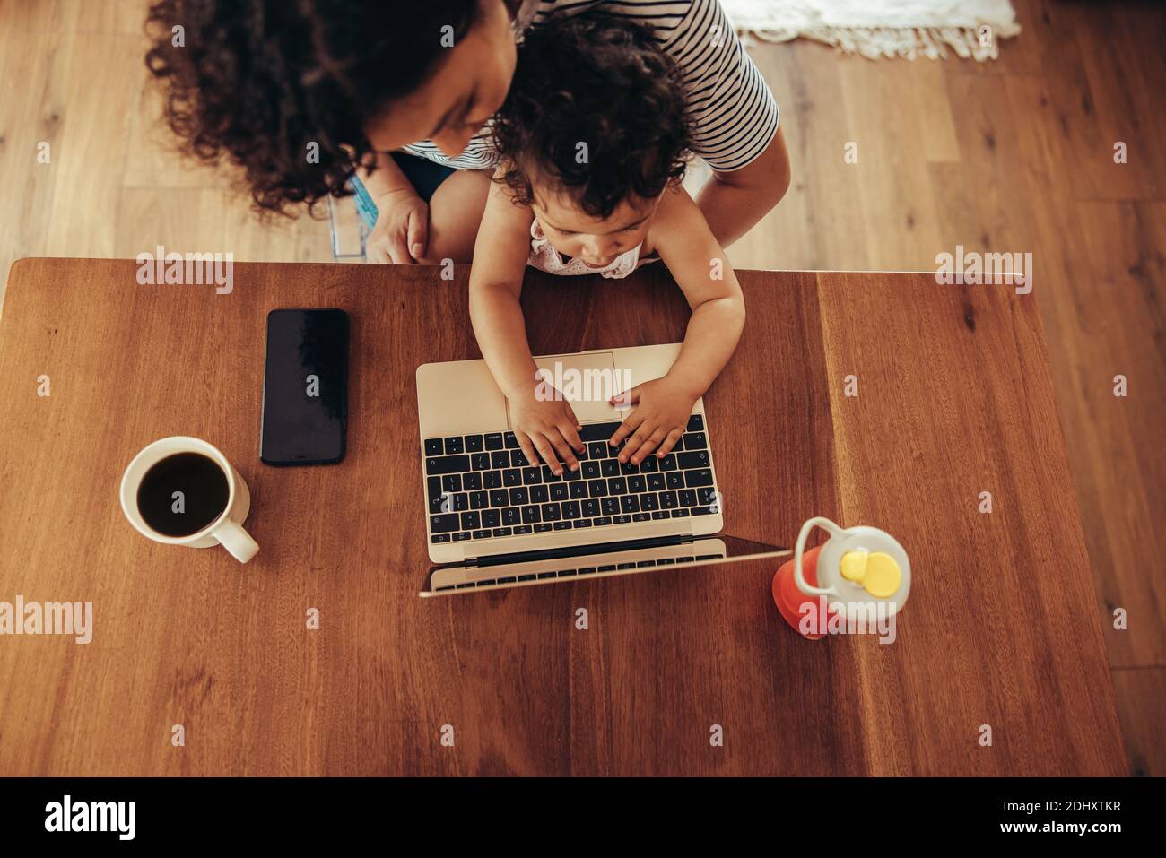 Vue de dessus d'une femme qui regarde son bébé à l'aide d'un ordinateur portable. Enfant assis sur les genoux de la mère et utilisant un ordinateur portable à la table. Banque D'Images