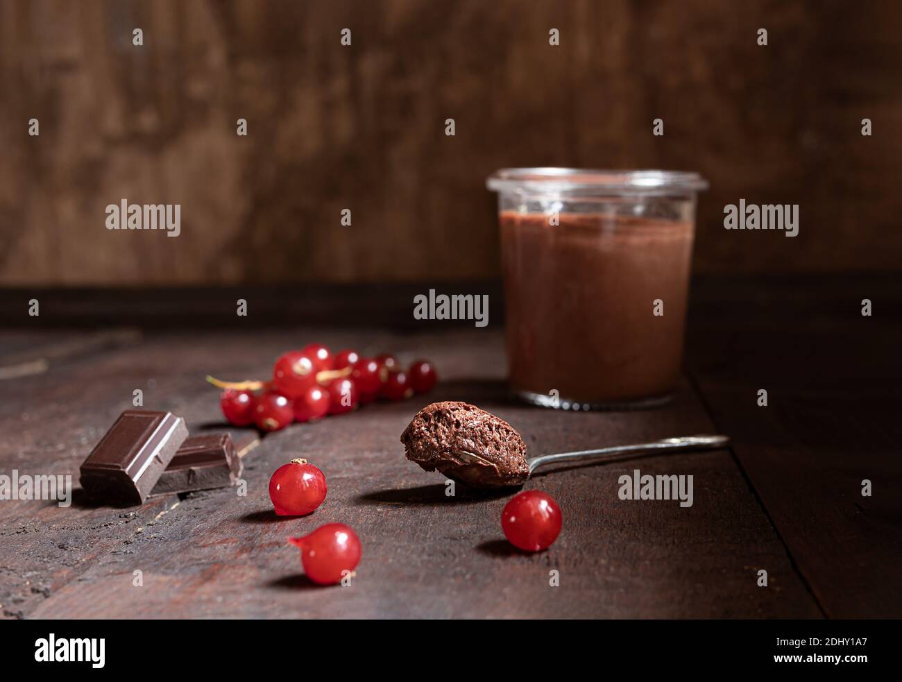Un verre et une cuillère à café avec mousse au chocolat, morceaux de chocolat noir et baies de cassis sur fond de bois Banque D'Images