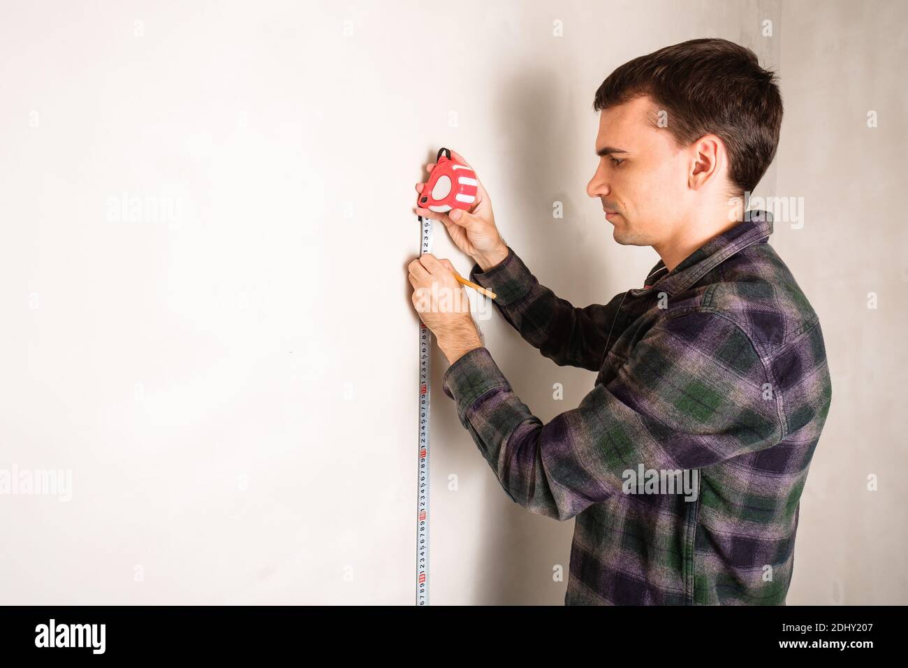 Homme de travail mesurant et marquant la distance sur le mur blanc avec mesurer l'outil à ruban et le crayon Banque D'Images