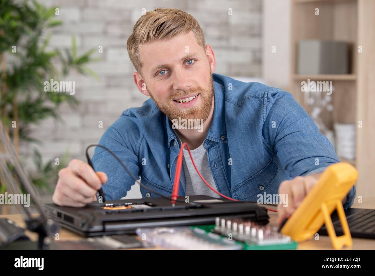 homme testant un ordinateur portable avec un multimètre Banque D'Images