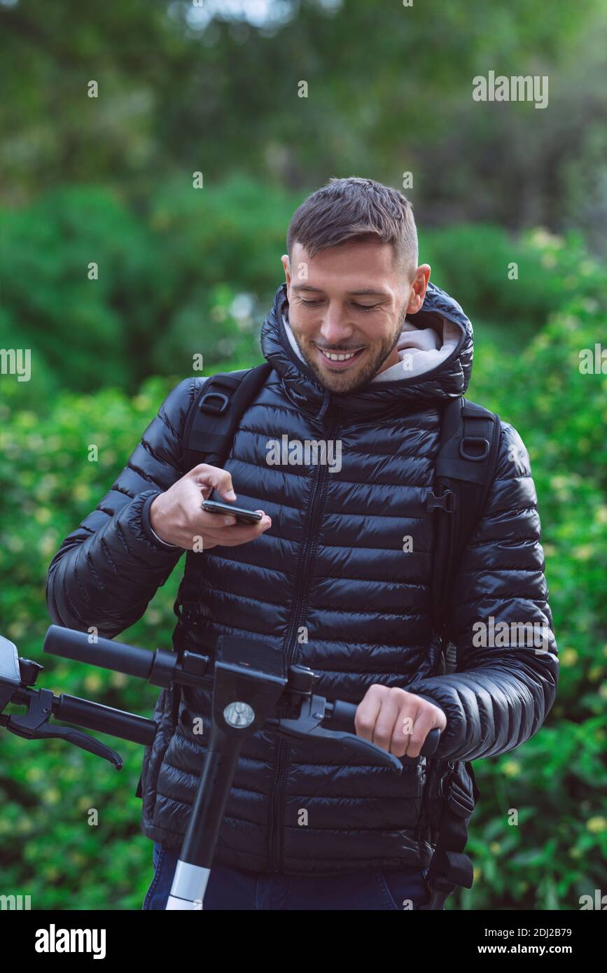 Jeune étudiant louant un scooter électrique avec un smartphone application Banque D'Images