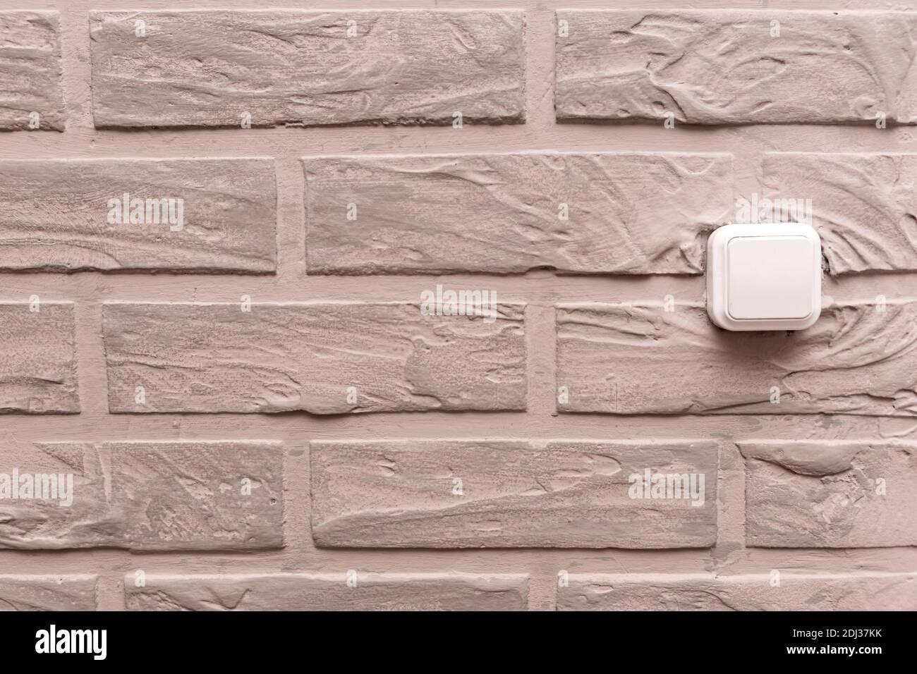 L'interrupteur électrique en plastique est situé sur le mur, décoré de plâtre décoratif beige sous forme de briques à l'intérieur. Banque D'Images