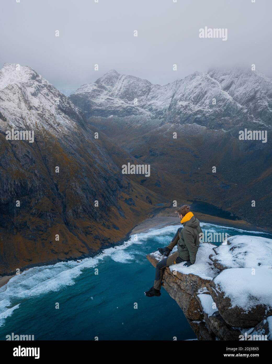 Homme assis sur une plate-forme d'observation sur une montagne en face de la plage de Kvalvika, Fredvang, Lofoten, Norvège Banque D'Images