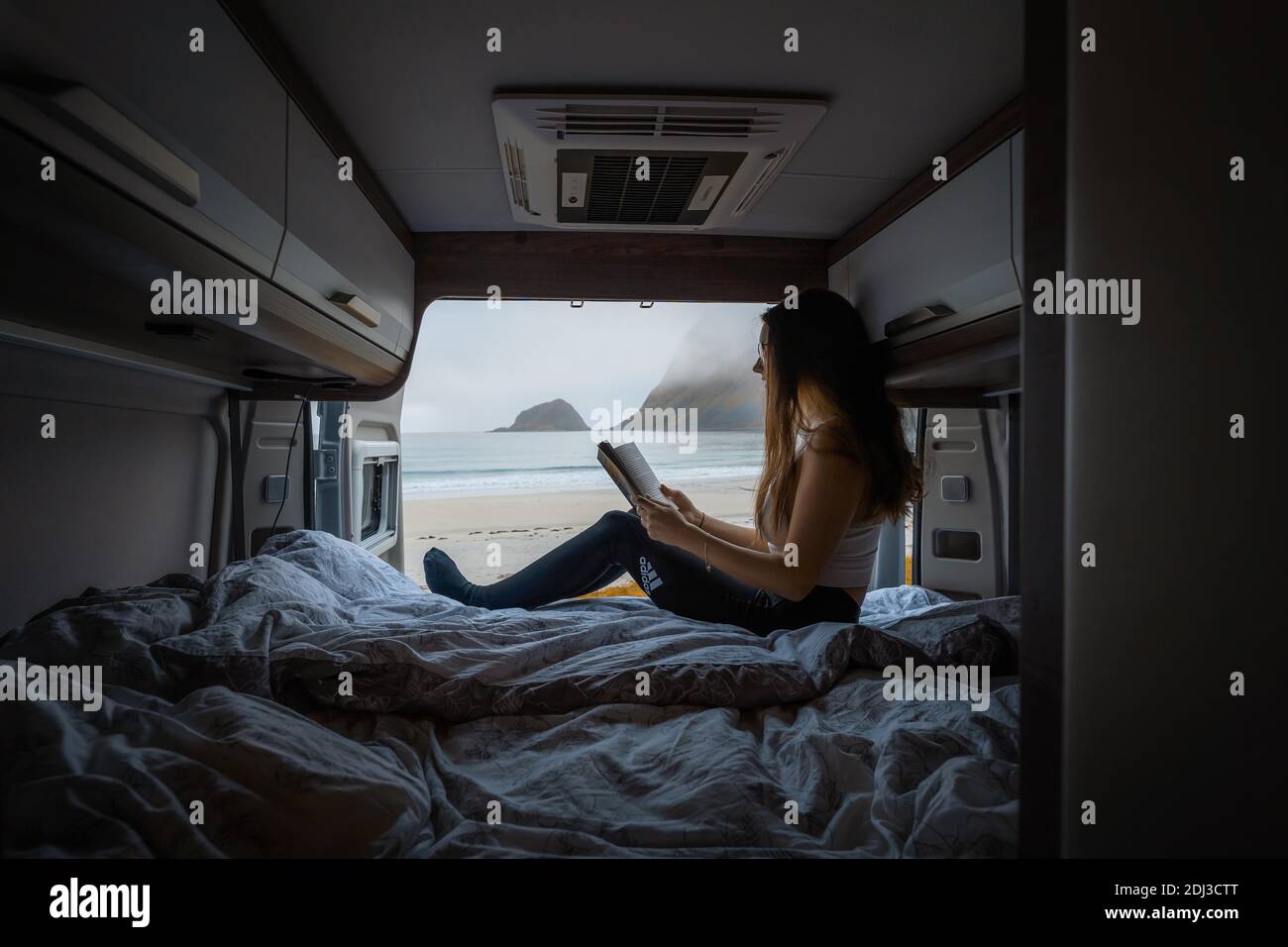 Frau lit en campervan avec vue de l'arrière du campervan sur la plage avec eau turquoise, plage Haukland, Lofoten, Norvège Banque D'Images