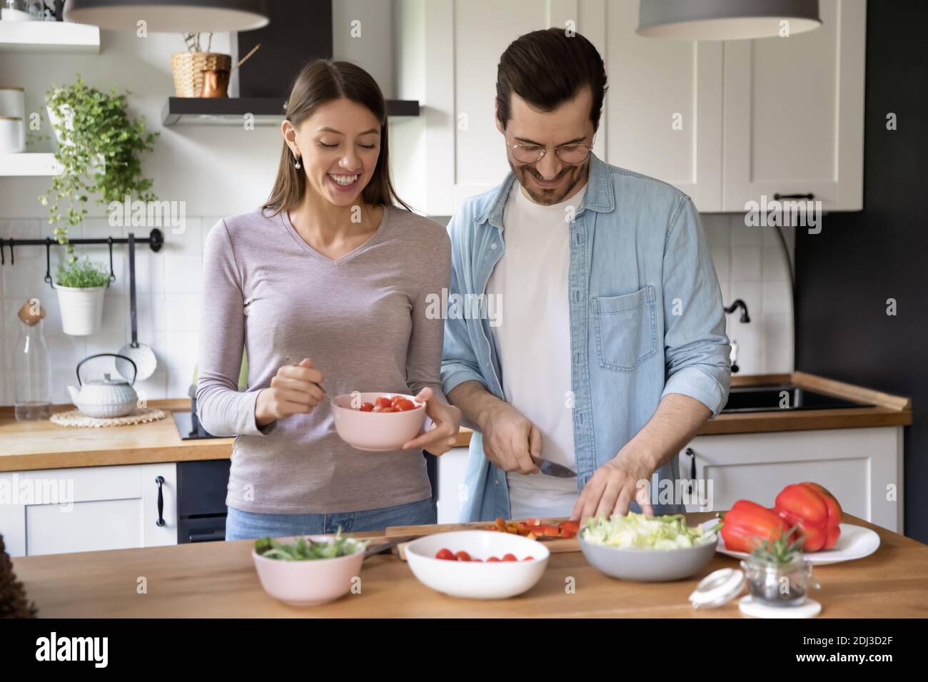 Joyeux jeune couple cuisant la salade ensemble, préparant le dîner à la maison Banque D'Images