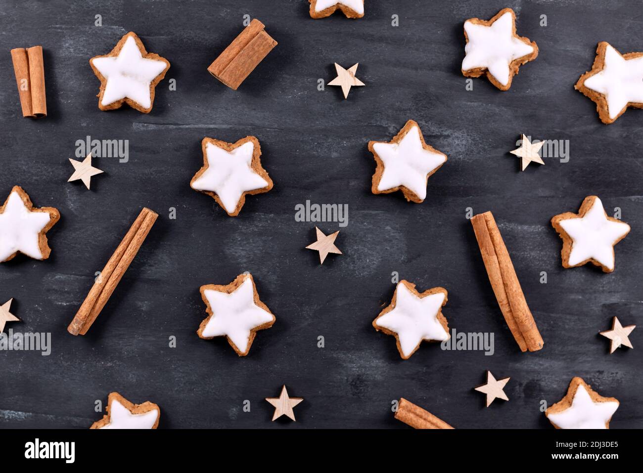 Biscuits de Noël traditionnels allemands en forme d'étoiles à la cannelle émaillée appelés « Zimtsterne » sur fond noir foncé avec ornements étoiles et bâtons de cannelle Banque D'Images
