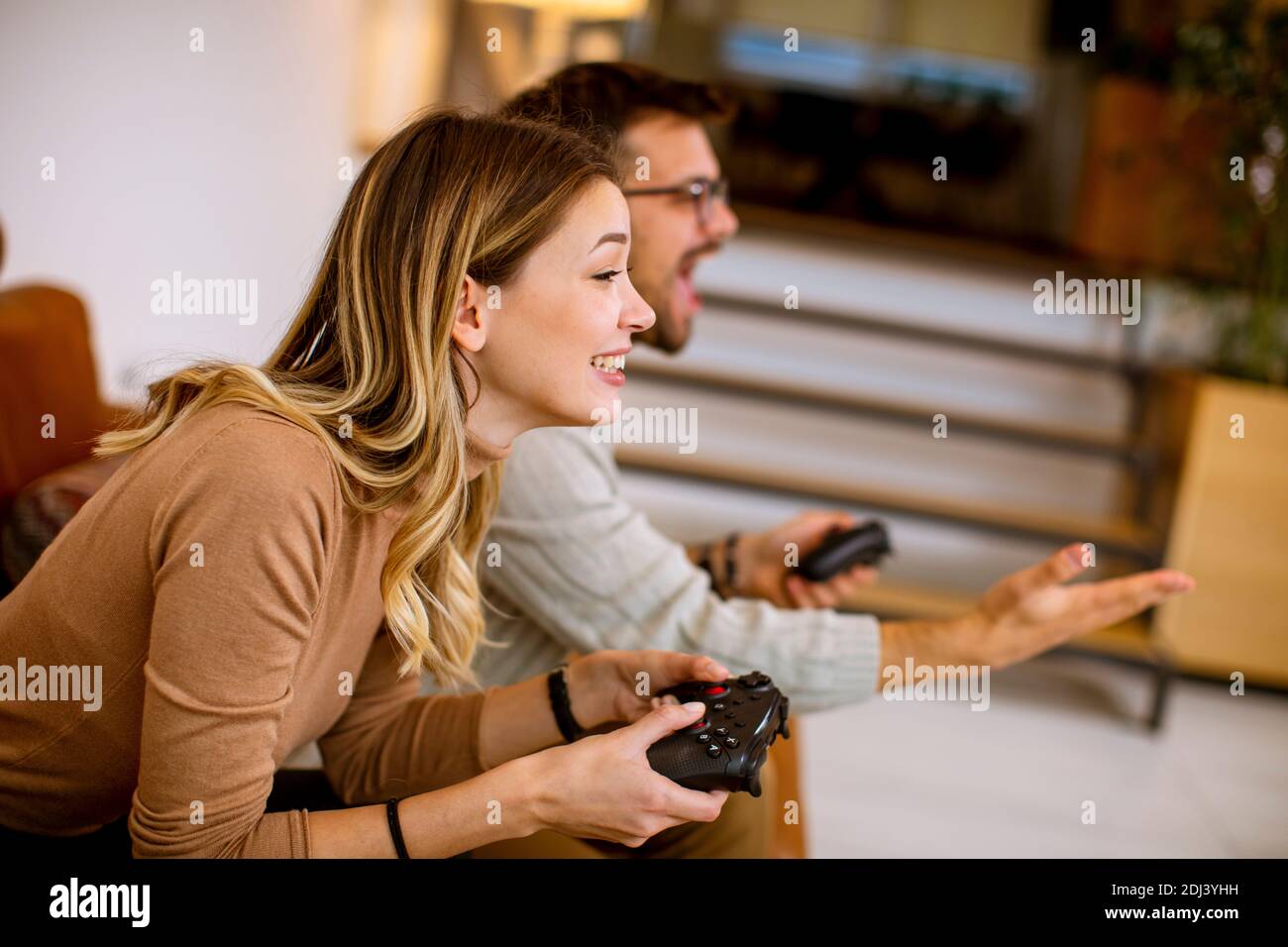 Beau jeune couple jouant à des jeux vidéo à la maison, assis sur un canapé et s'amuser Banque D'Images