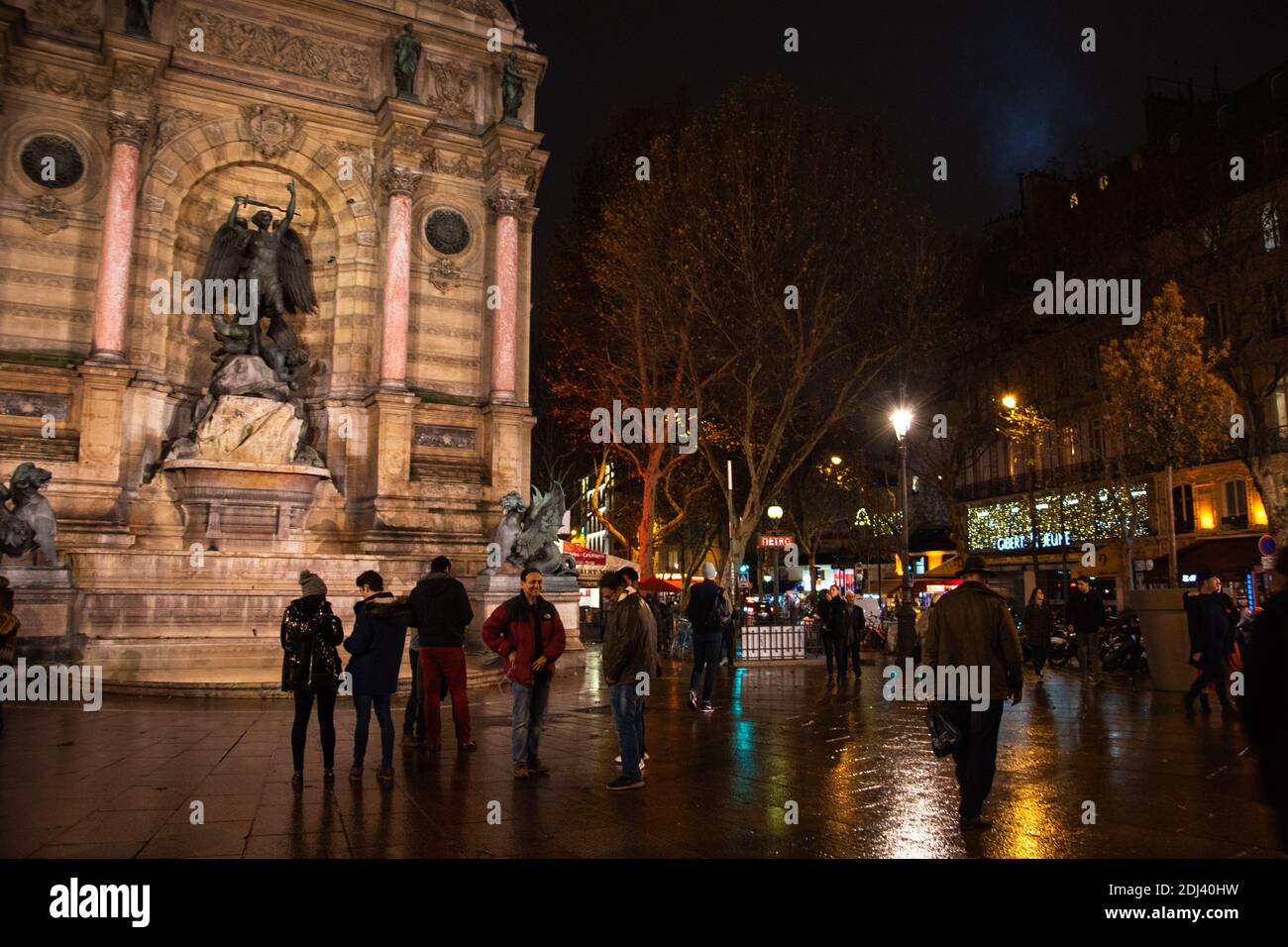PARIS, FRANCE - 2 DÉCEMBRE 2018 : Tourisme et rencontres locales sur la place Saint Michel le soir. Réflexion colorée des lumières sur l'eau (après la pluie) Banque D'Images