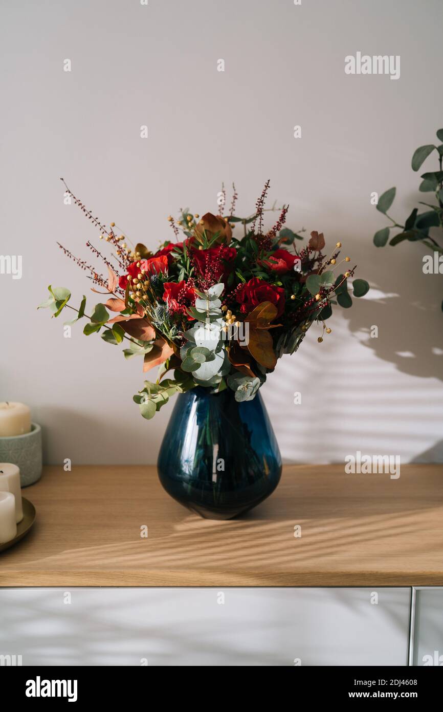 Bouquet de fleurs rouges par fleuriste avec roses rouges, coquelicots et feuilles d'eucalyptus dans un vase bleu sur une table en bois Banque D'Images