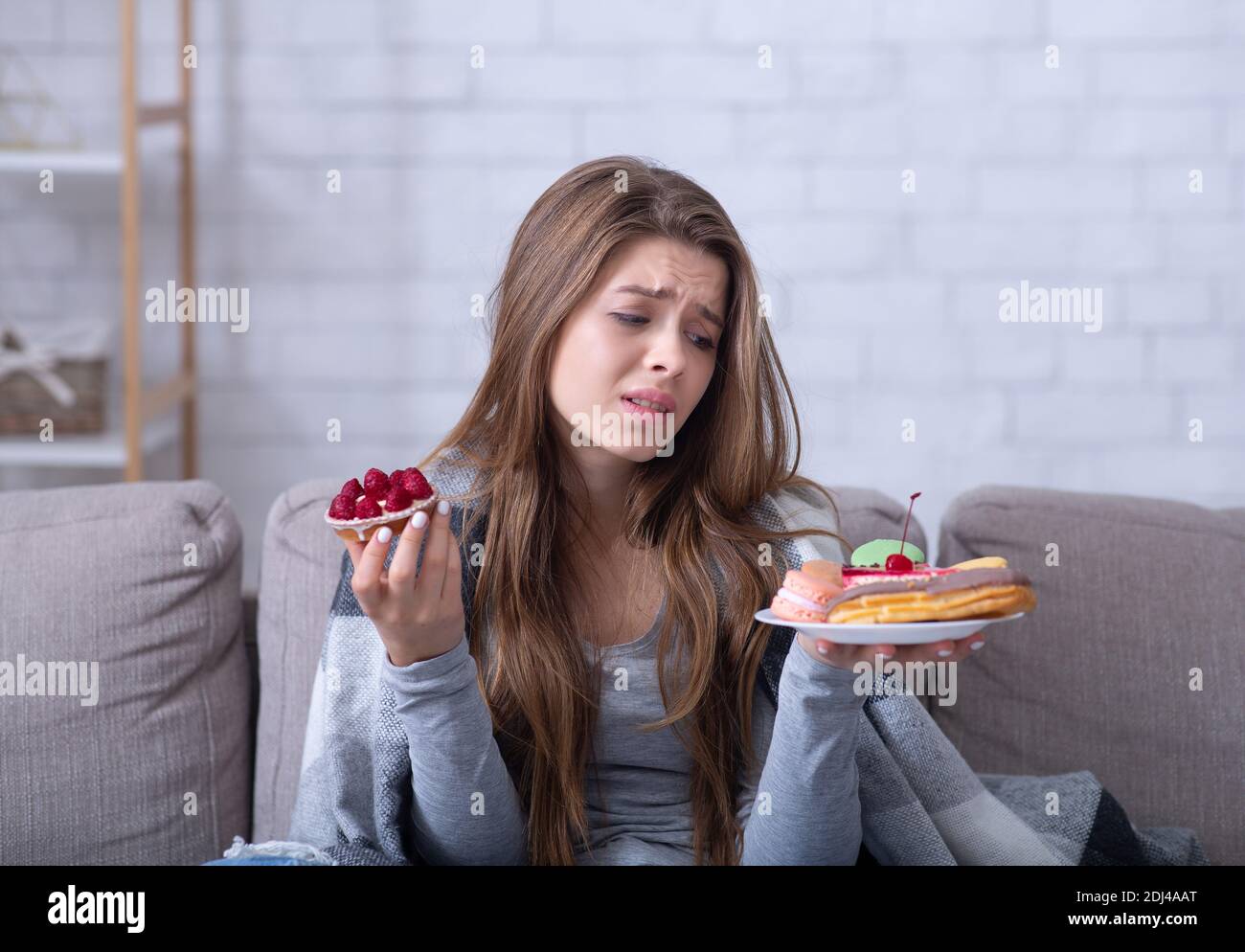 Une jeune femme dépressive ayant des troubles de l'alimentation, se réconfortant avec des bonbons sur le canapé à la maison Banque D'Images