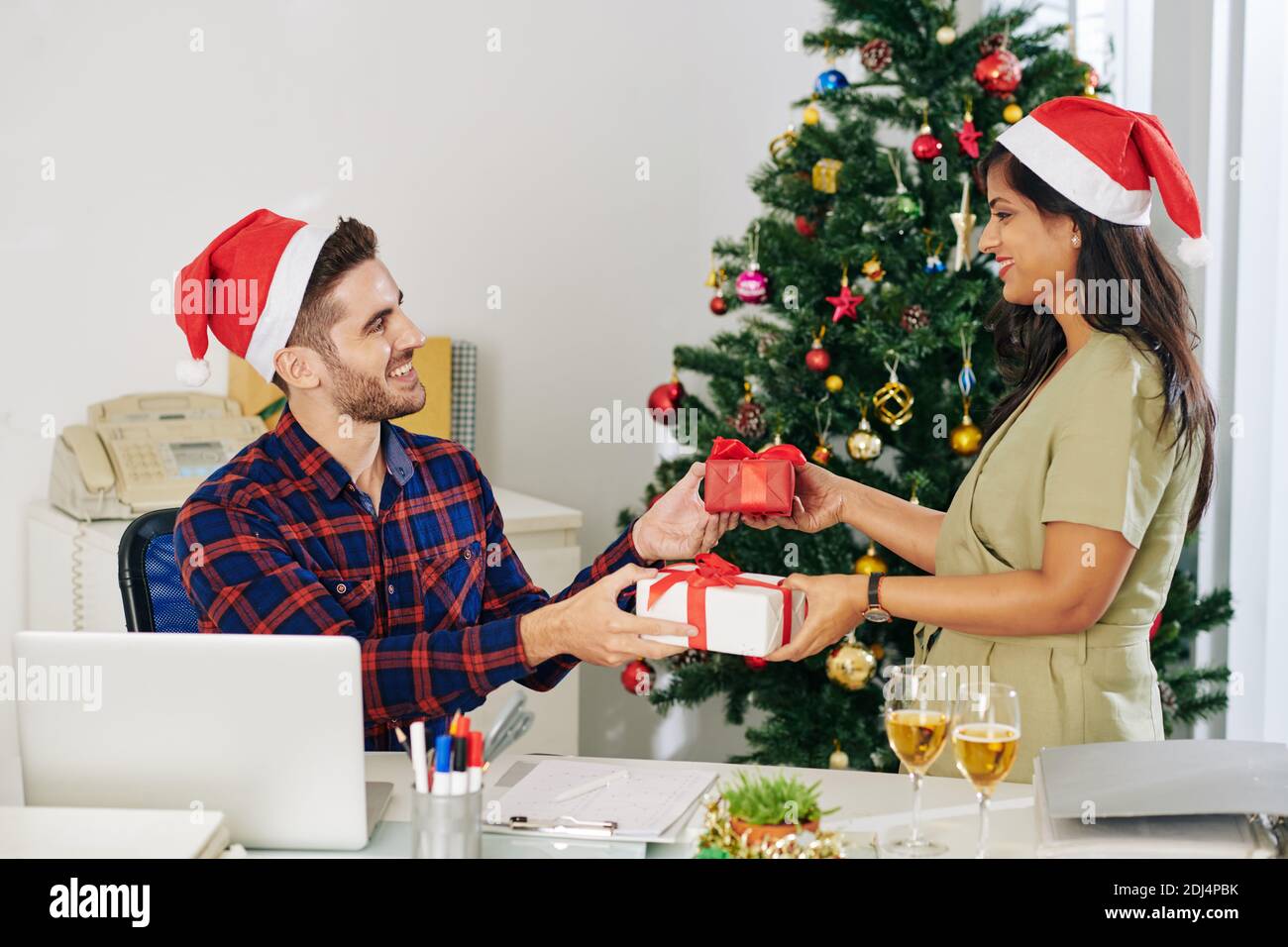 Des jeunes collègues souriants entre les mains du Père Noël échangeant des cadeaux de Noël au bureau Banque D'Images